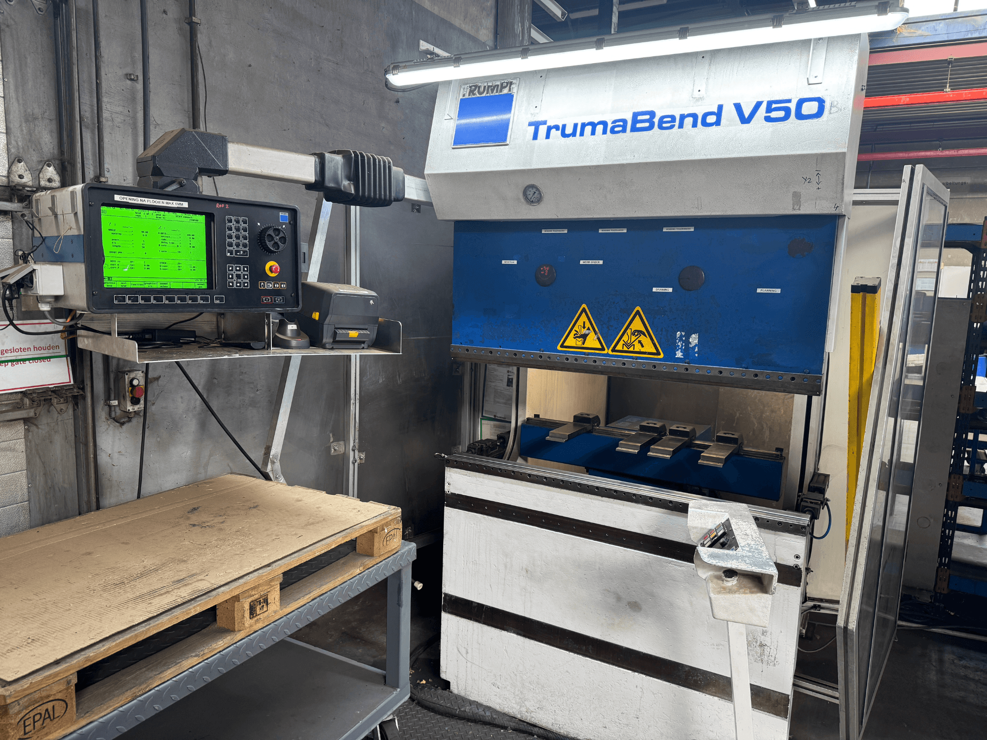 Travão de prensa TRUMPF TrumaBend V50, vista frontal, com painel de controlo que apresenta definições e sinais de aviso de segurança.