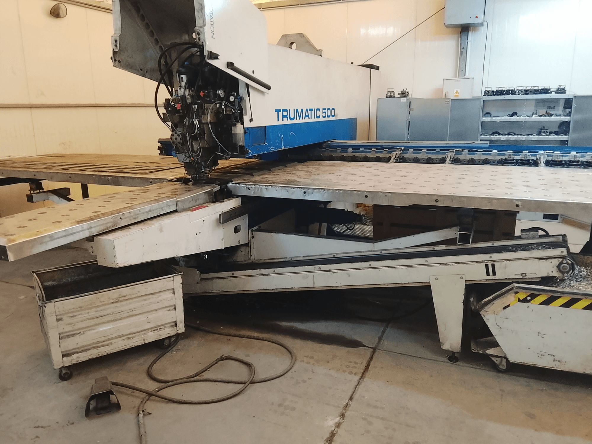 Máquina CNC TRUMATIC 500 numa oficina, vista lateral mostrando a cabeça de corte e a mesa de trabalho metálica com furos pré-perfurados.