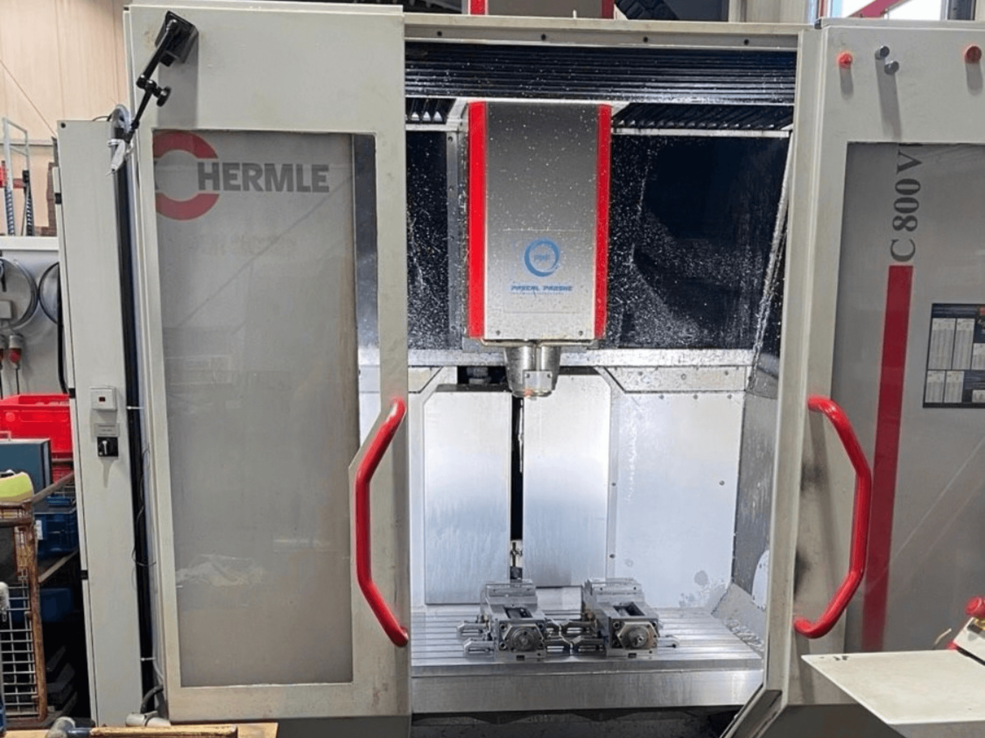 Centro de maquinagem vertical HERMLE C800V, vista frontal que mostra a área de maquinagem com as peças de trabalho e o líquido de arrefecimento.