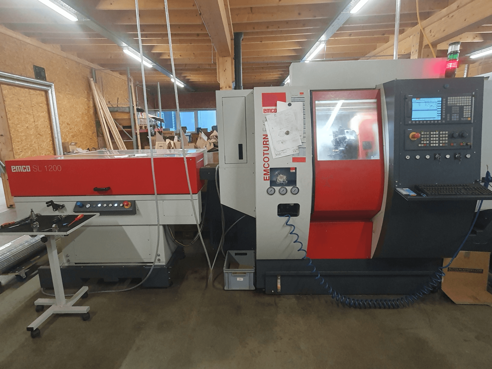 Torno CNC EMCO SL 1200 e EMCOturn; vista frontal mostrando os controlos, ecrãs e indicadores operacionais numa oficina.
