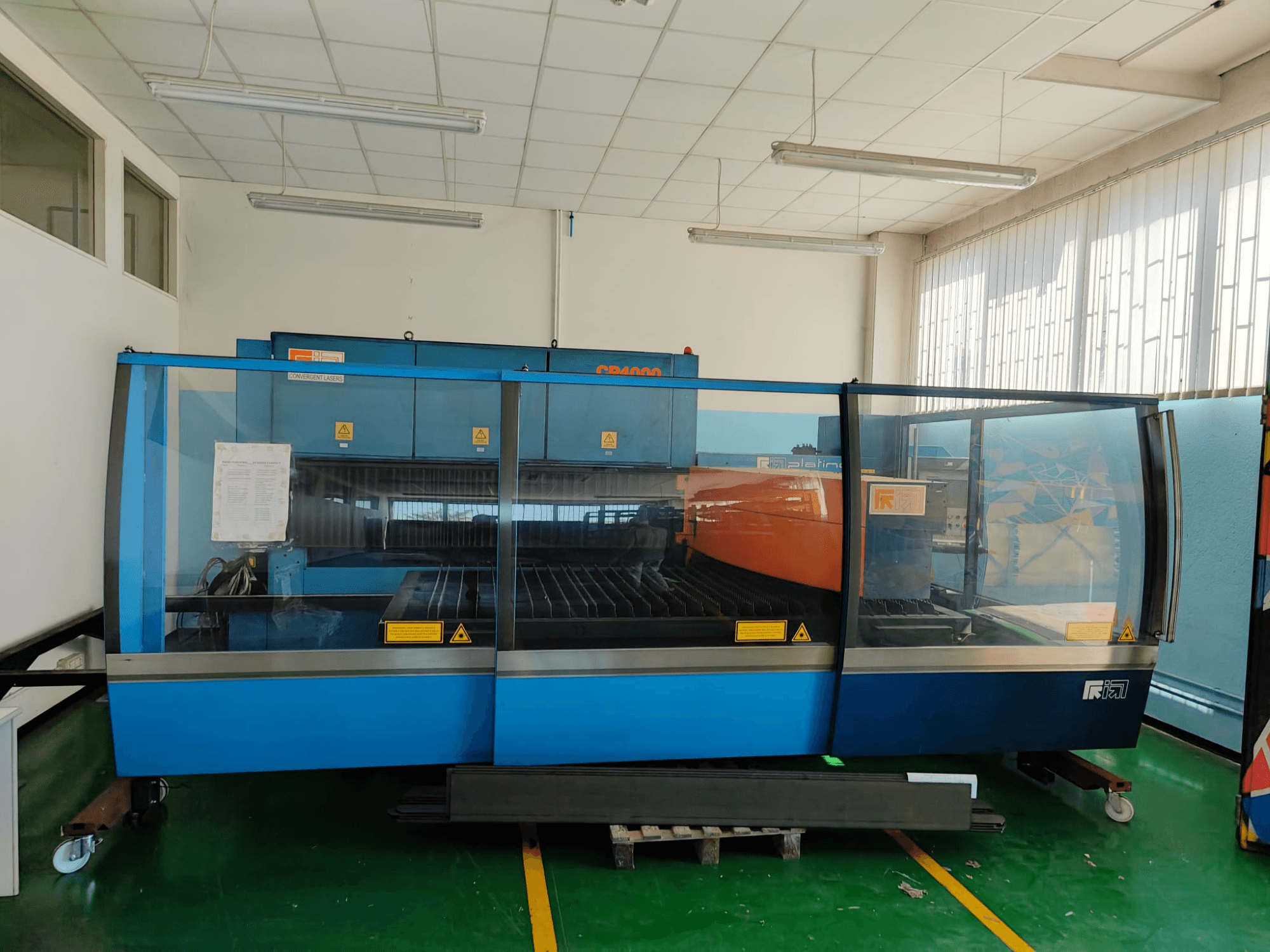 Vista frontal de uma máquina de corte a laser de CO₂ CONVERGENT LASERS CP4000, com um design em azul e laranja, num ambiente de oficina bem iluminado.
