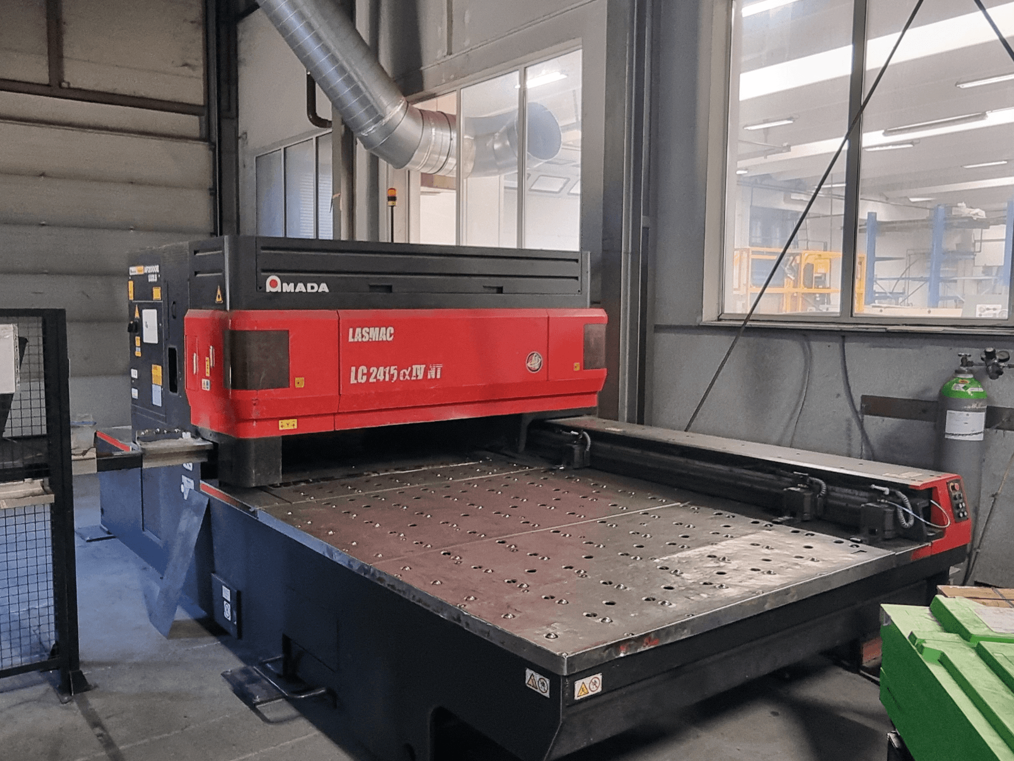 Máquina de corte a laser Amada LASMAC LC 2415 αⅡ NT em vermelho e preto, vista frontal, com uma base de corte motorizada e controlos de precisão.