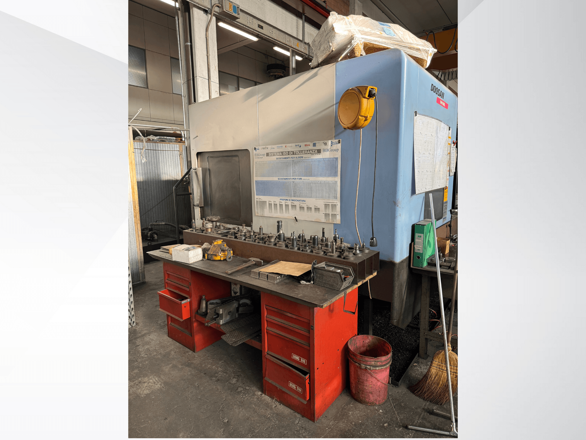 Centro de maquinagem Doosan com uma bancada de trabalho e arrumação vermelha, com ferramentas e equipamento, visto de frente.