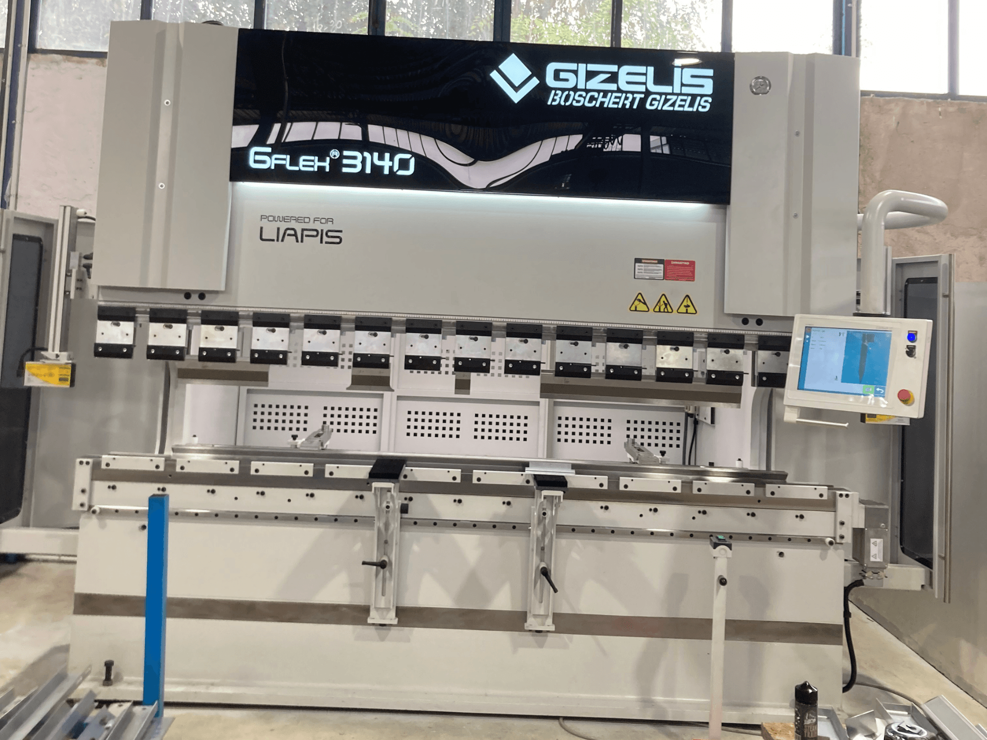 Prensa hidráulica GIZELIS G-FLEX 3140 em vista frontal com ecrã de controlo, com várias ferramentas de dobragem e etiquetas de segurança.