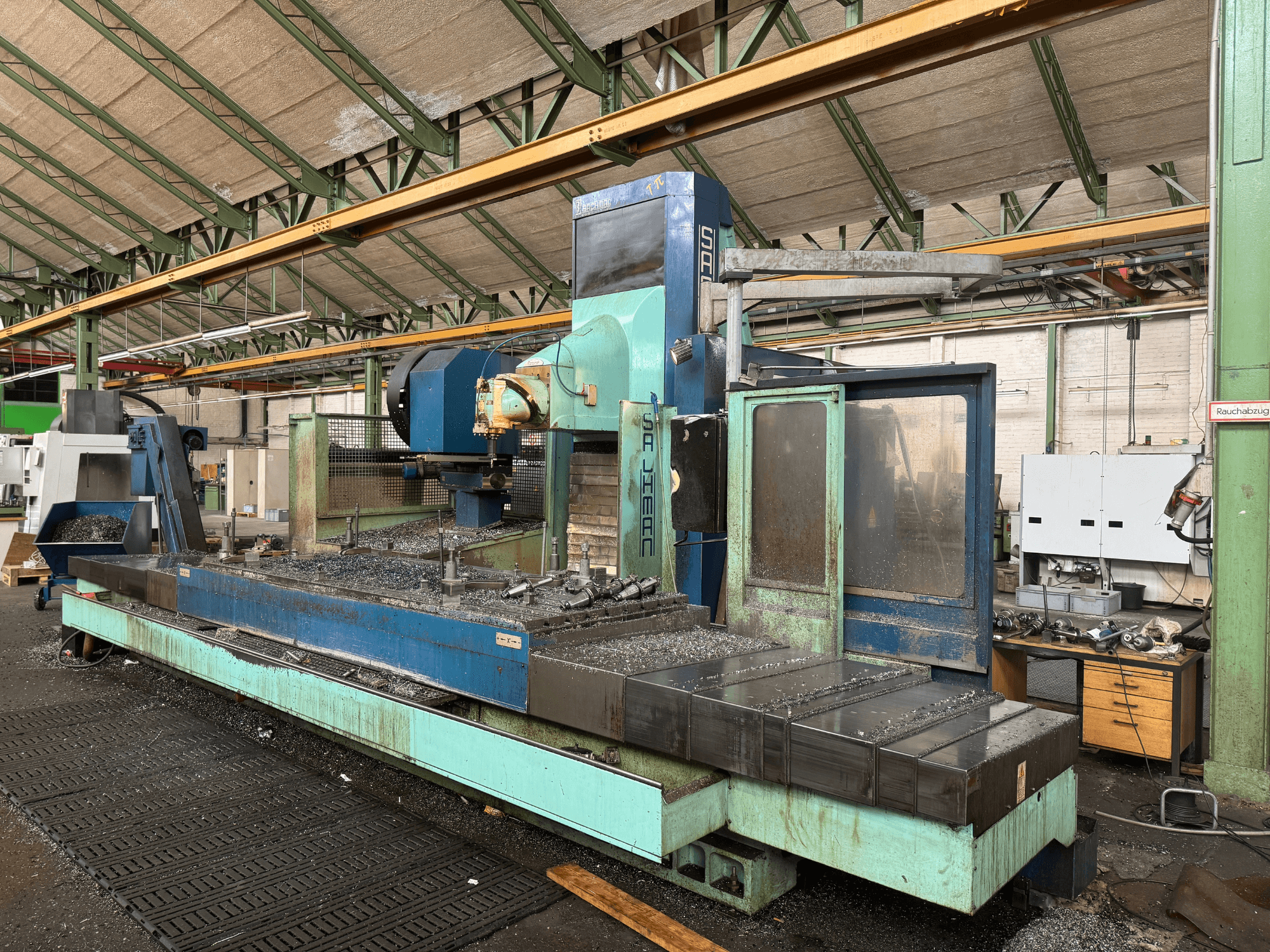 Fresadora Salvador em ambiente fabril, vista frontal, com esquema de cores azul e verde, mostrando aparas de metal na base.