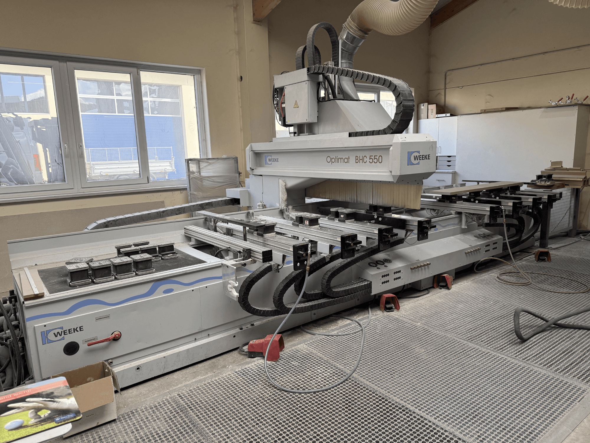 Centro de maquinação CNC para madeira Weeke Optimat BHC 550, vista frontal mostrando a cabeça da ferramenta e a mesa de trabalho, com o sistema de extração de poeiras visível.