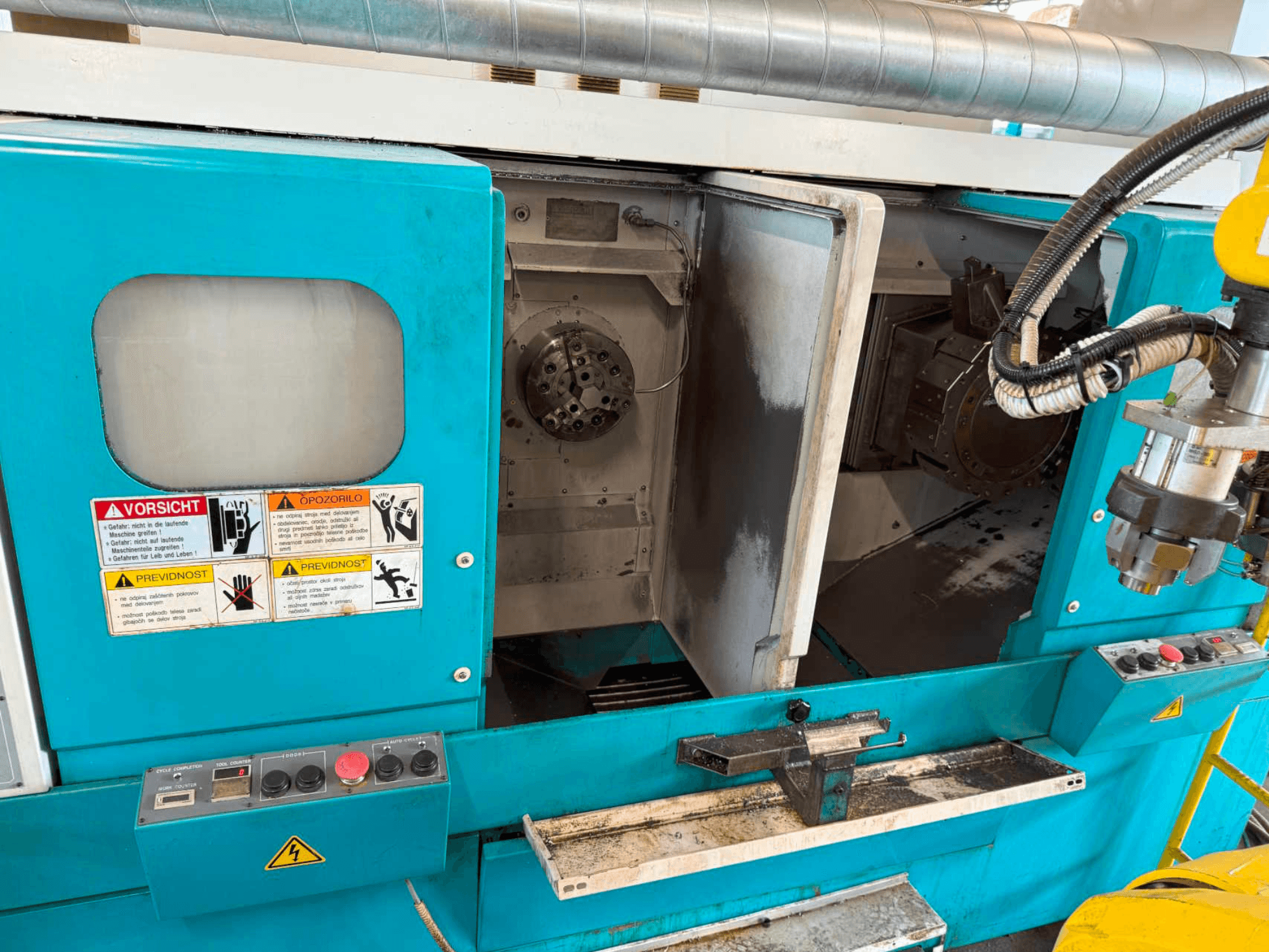 Torneiro horizontal DOOSAN H310T, vista frontal mostrando o painel de controlo e a área do fuso com avisos de segurança.