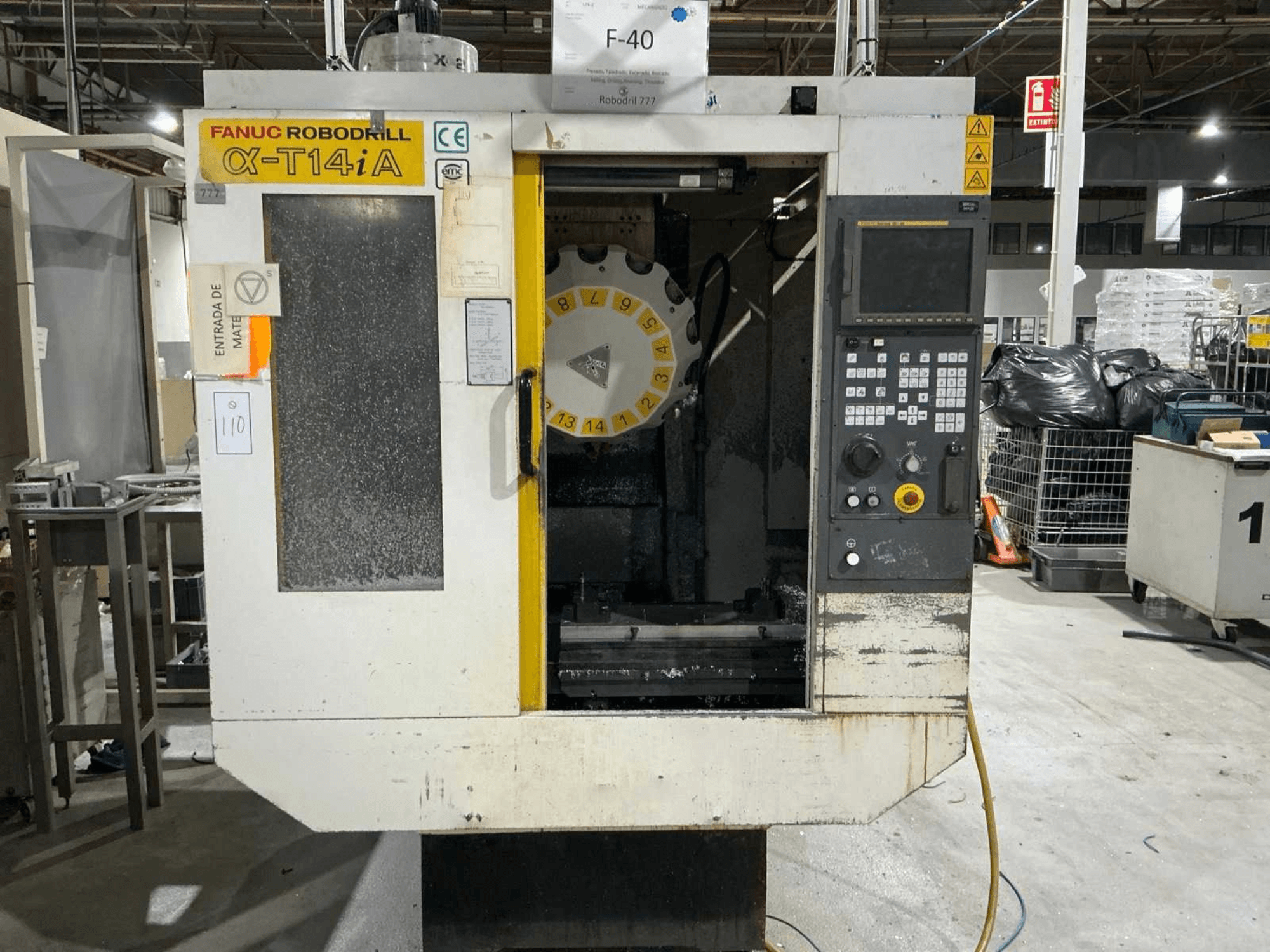 Centro de maquinação vertical FANUC ROBODRILL α-T14iB, vista frontal mostrando o painel de controlo e o carrossel de ferramentas.