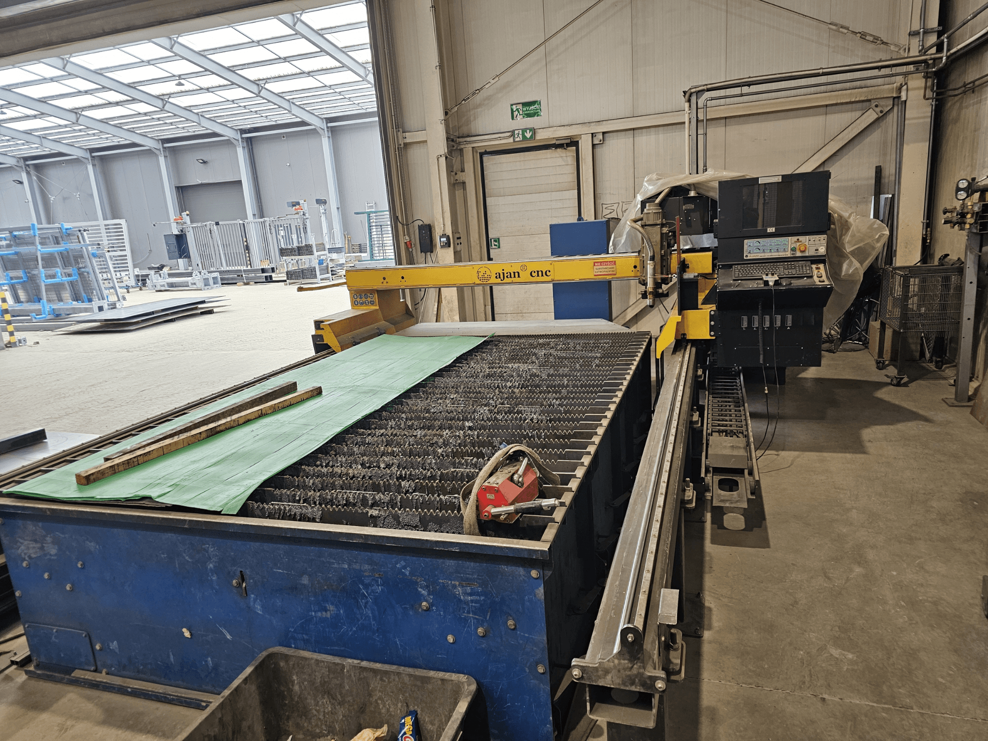 AJAN PP16011 Máquina de corte por plasma automática em vista lateral, com uma mesa de corte e um painel de controlo, inserida num ambiente de oficina.