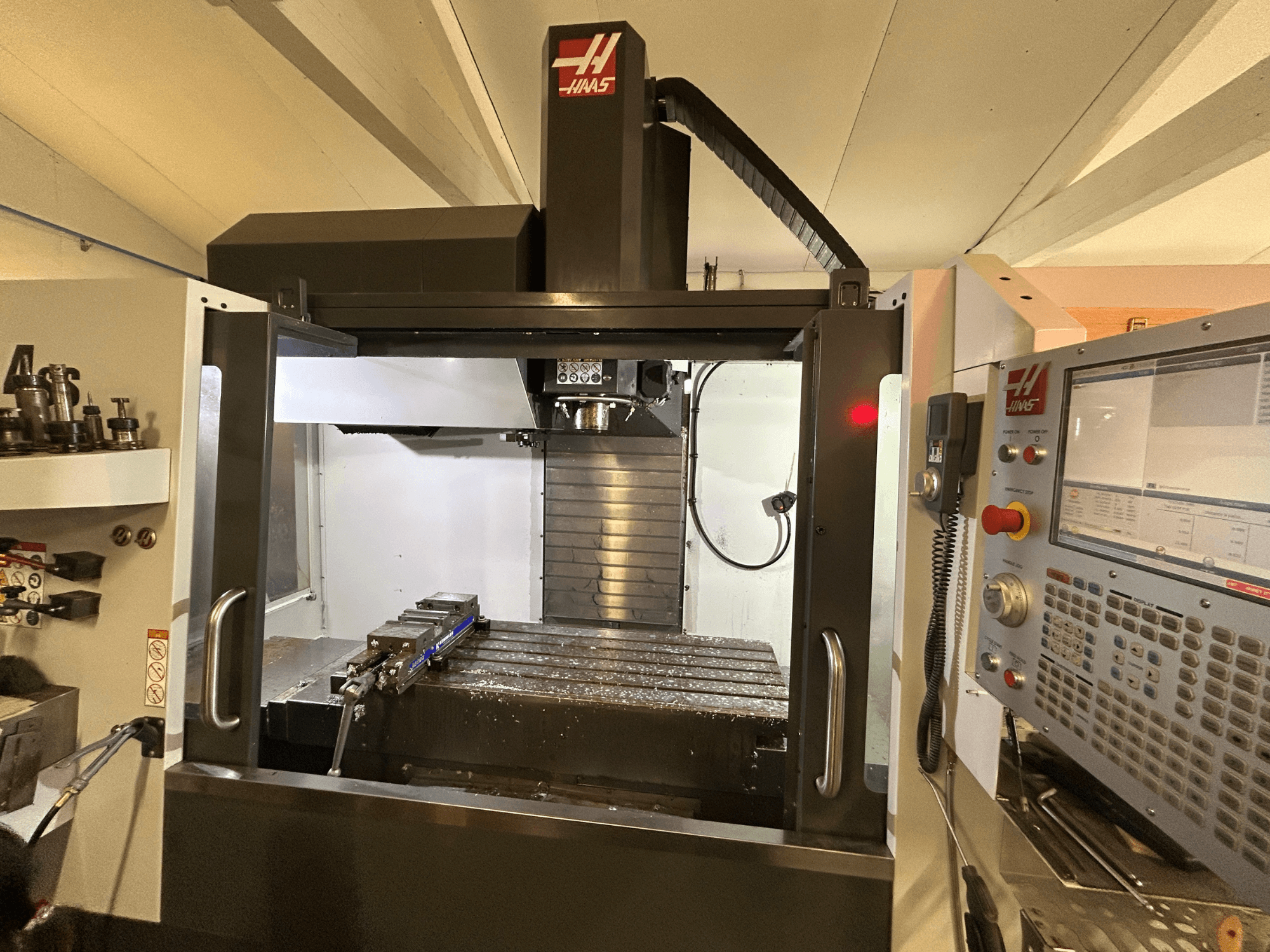 Centro de maquinação vertical HAAS VF-4SS, vista frontal, mostrando o painel de controlo, o suporte de ferramentas e a área de trabalho com aparas de metal.