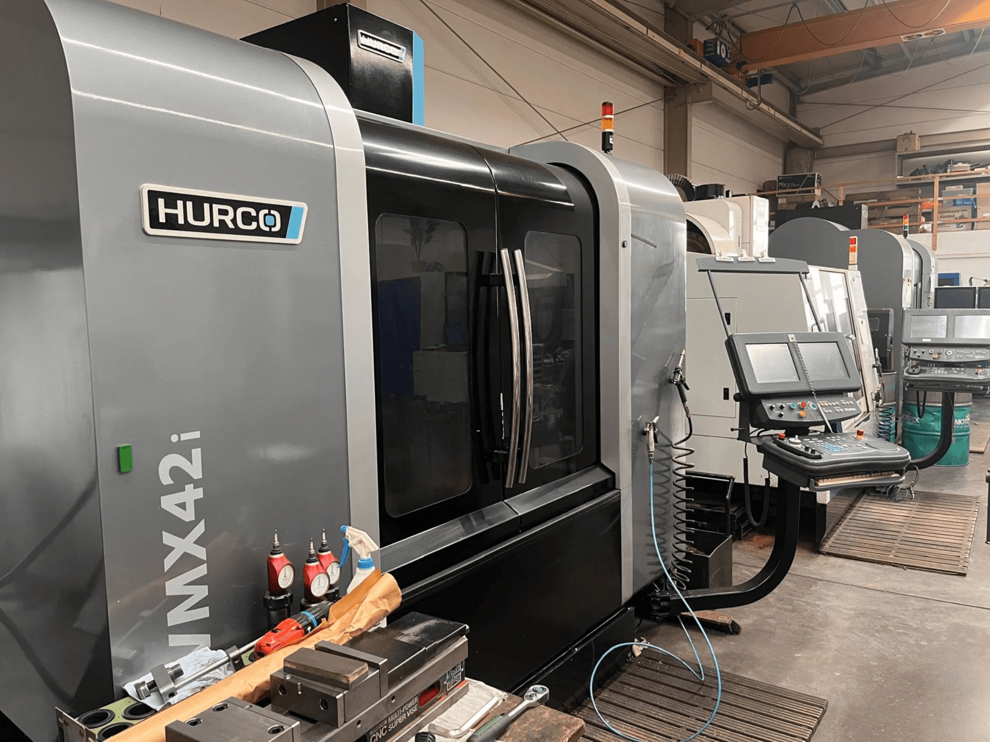 Máquina CNC Hurco VMX42i numa oficina, vista frontal, com painel de controlo e várias ferramentas na bancada de trabalho.