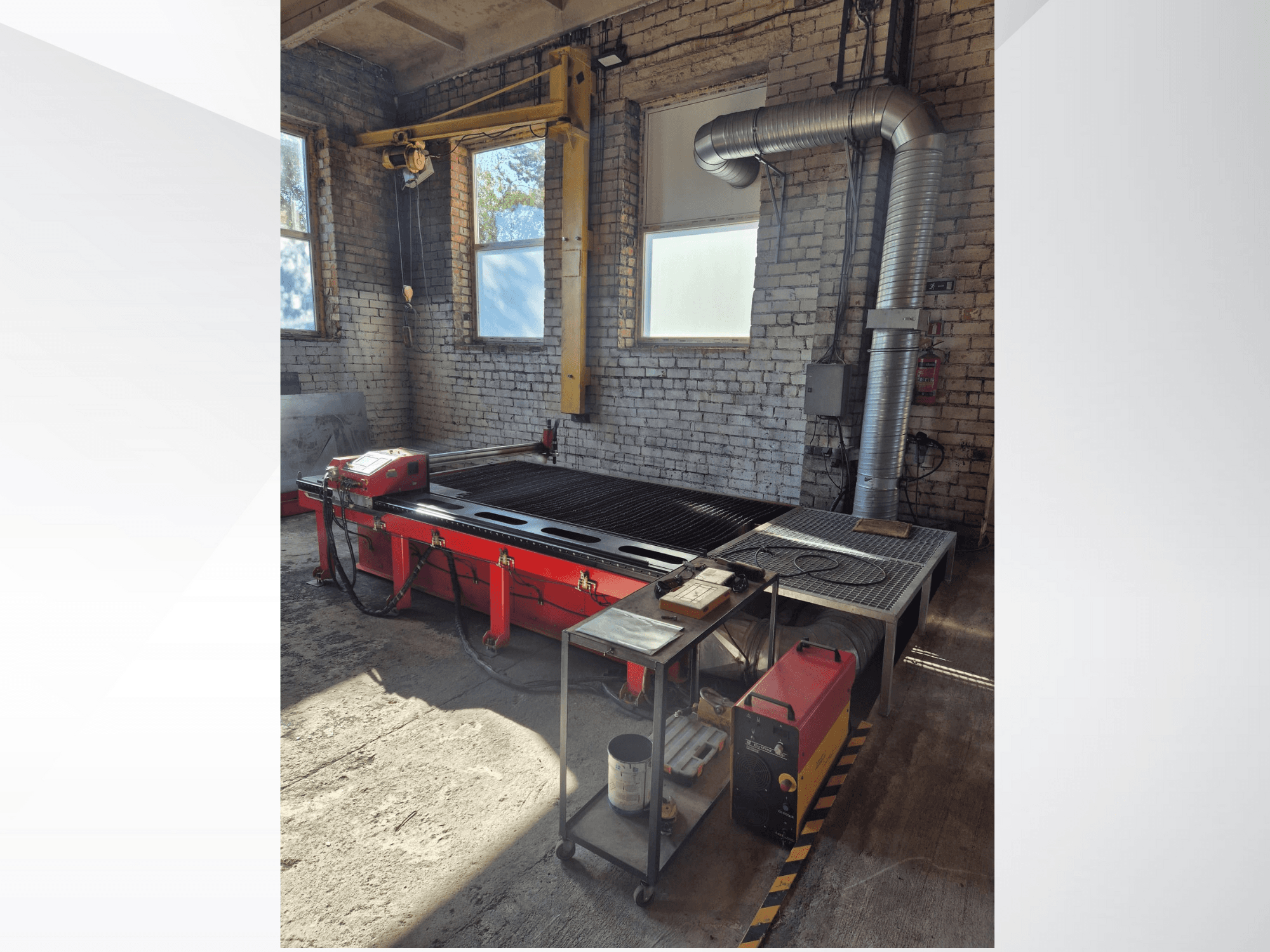Mesa de corte plasma CNC vermelha com painel de controlo e conduta de exaustão metálica, vista de lado numa oficina bem iluminada.