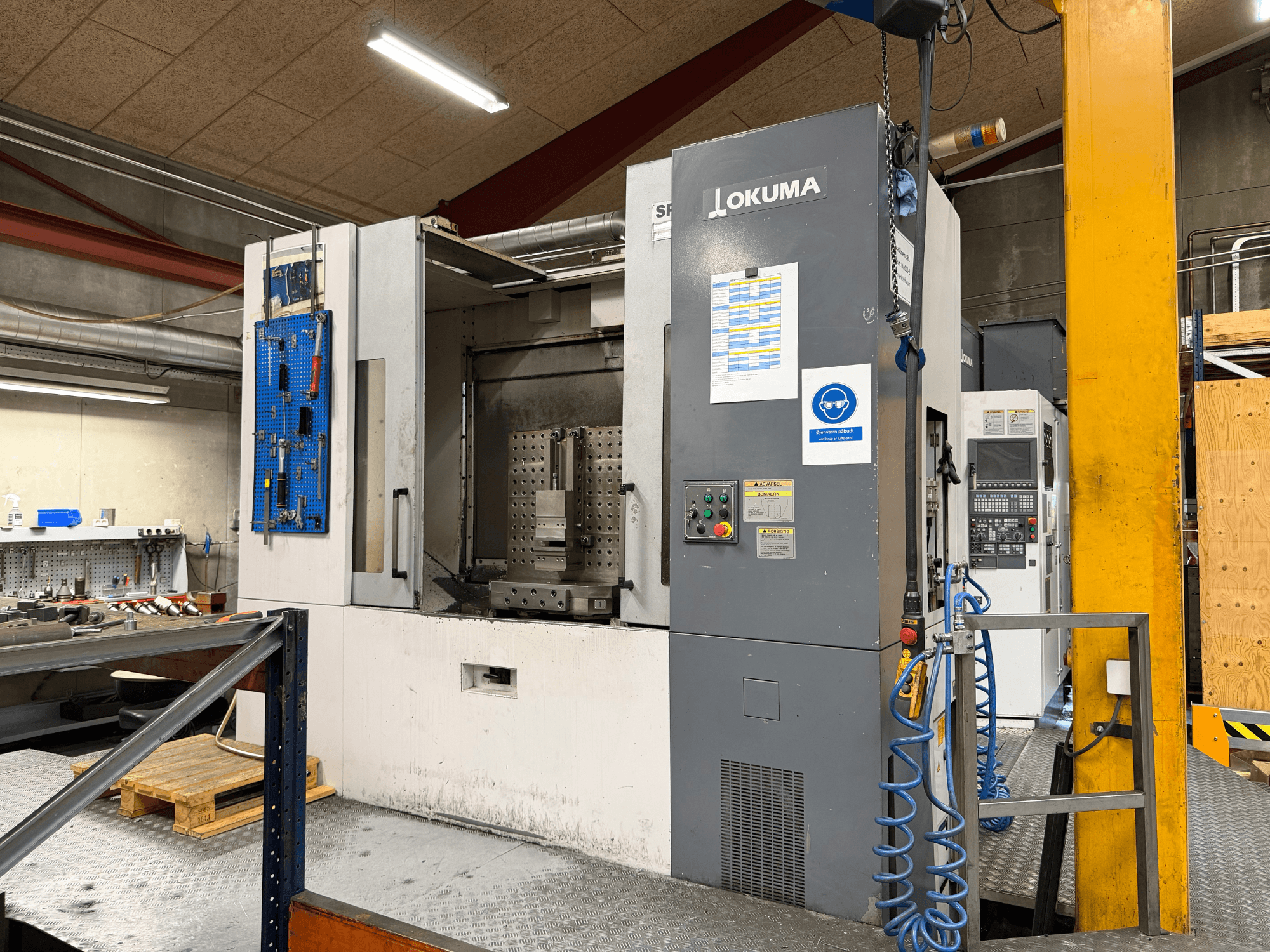 Centro de maquinagem horizontal Okuma MA-600HB numa oficina, vista frontal que mostra o painel de controlo e a área de trabalho.