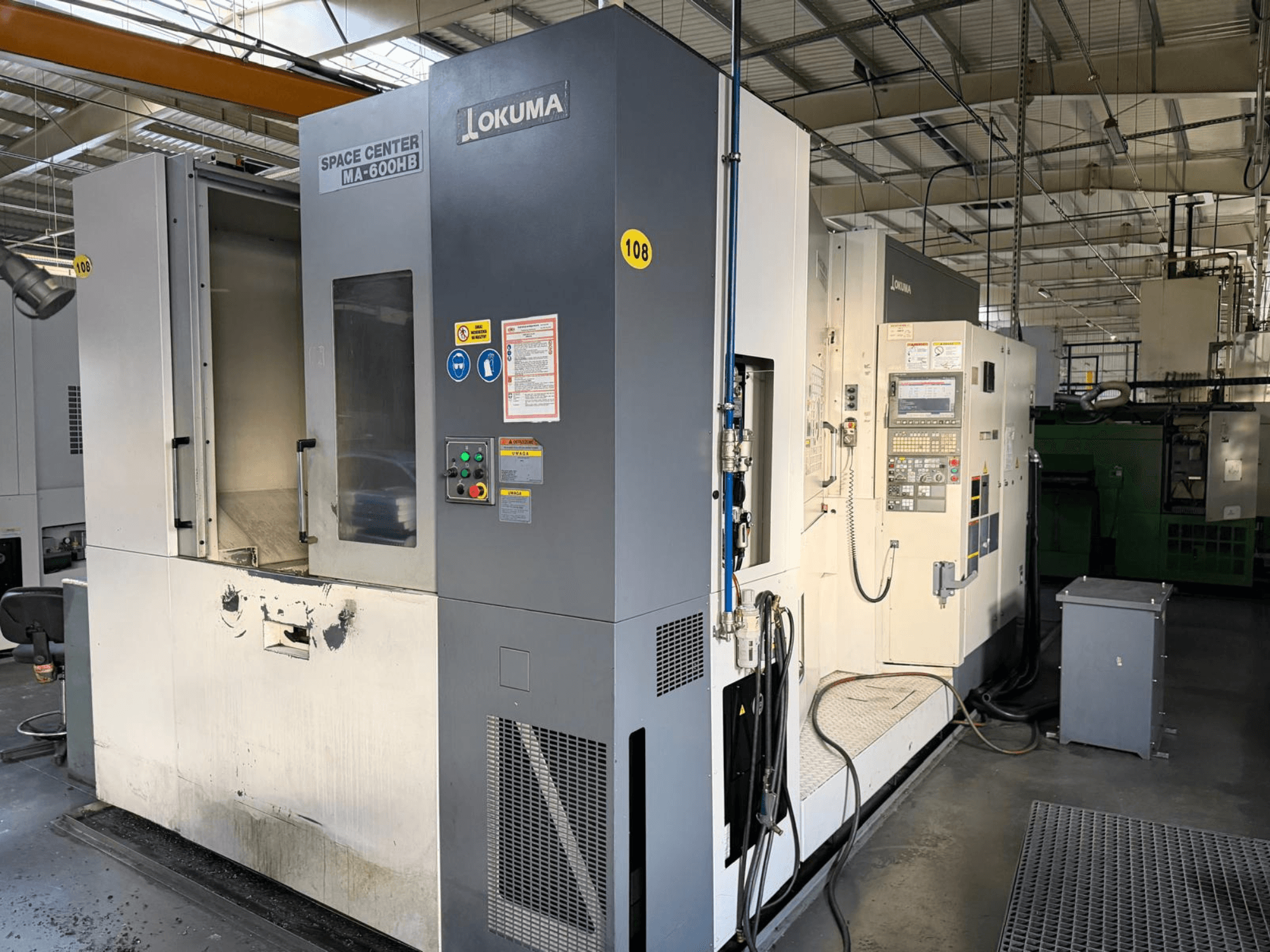 Centro de maquinação horizontal Okuma MA-600 HB, vista frontal, mostrando o painel de controlo e a área de corte com marcas de desgaste visíveis.