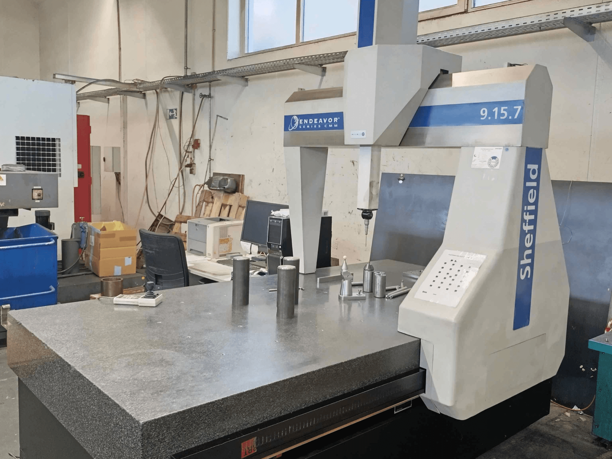 Máquina de medição por coordenadas Sheffield Endeavor 9.15.7 numa oficina, com uma mesa de granito e peças metálicas.