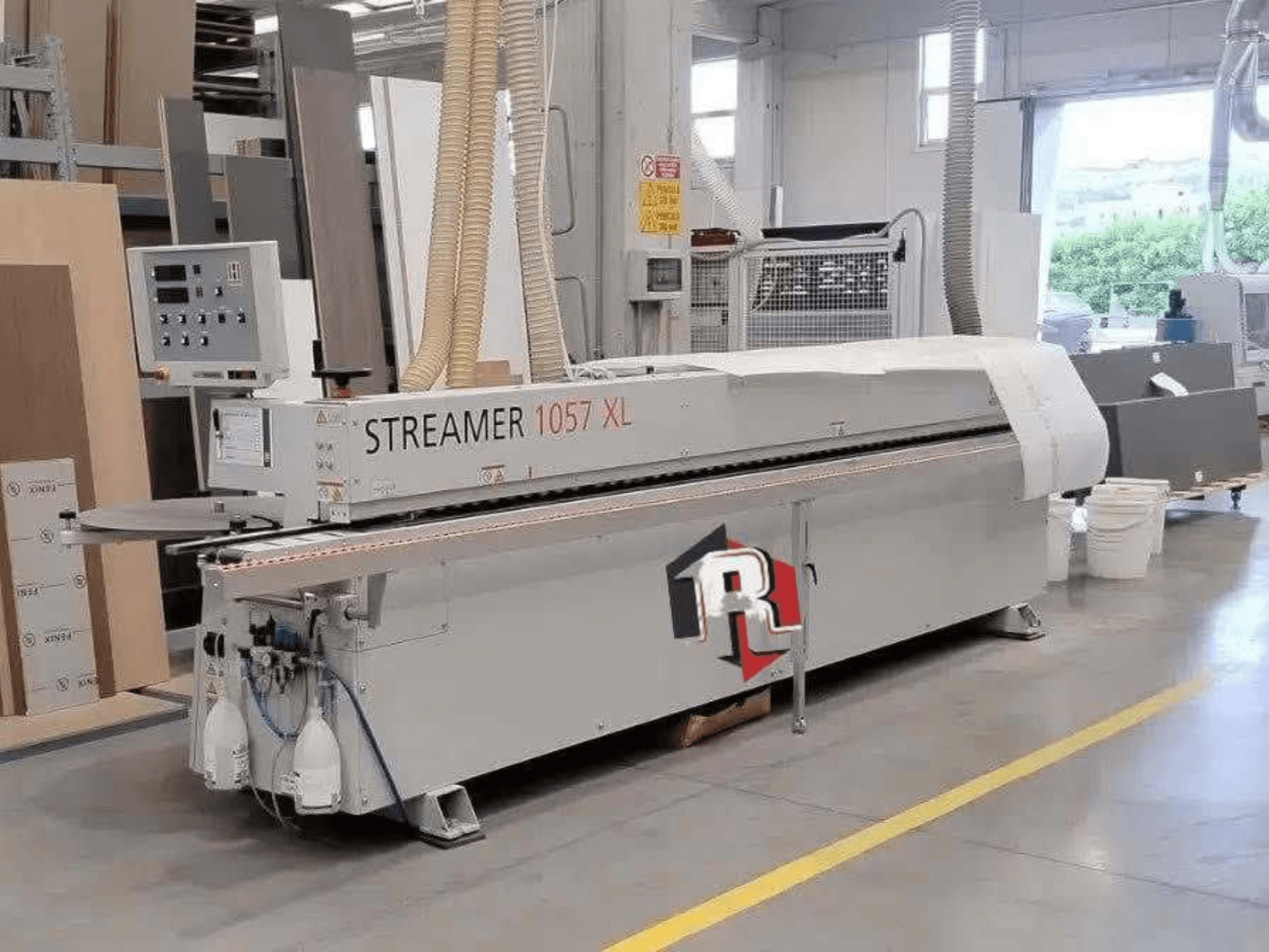 Máquina de encadernação HOLZHER STREAMER 1057 XL numa oficina, vista lateral com o painel de controlo e as mangueiras de ar visíveis.