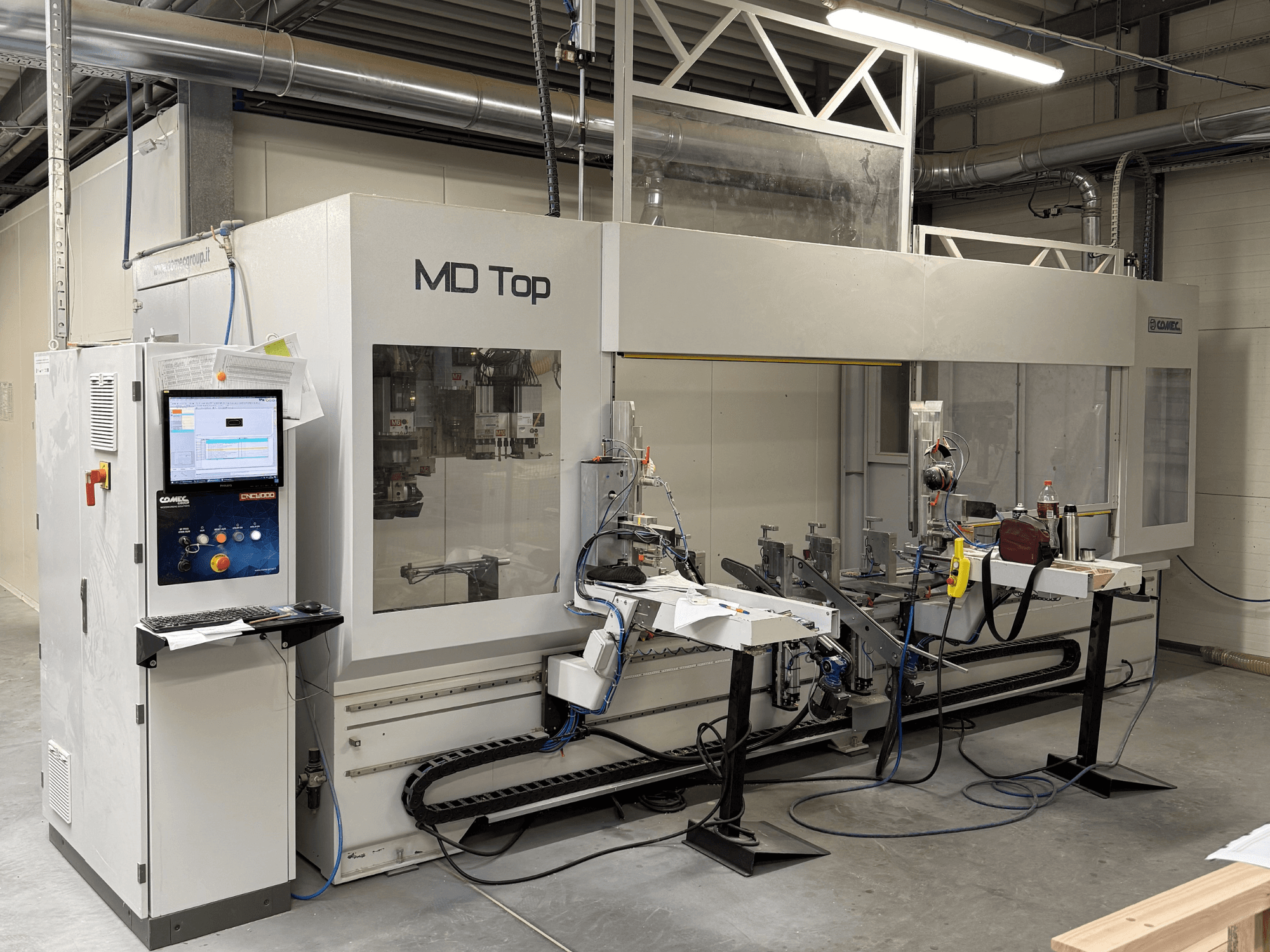 MD Top Máquina CNC vista de frente, com um painel de controlo, braços robóticos e espaço de trabalho com ferramentas e materiais.