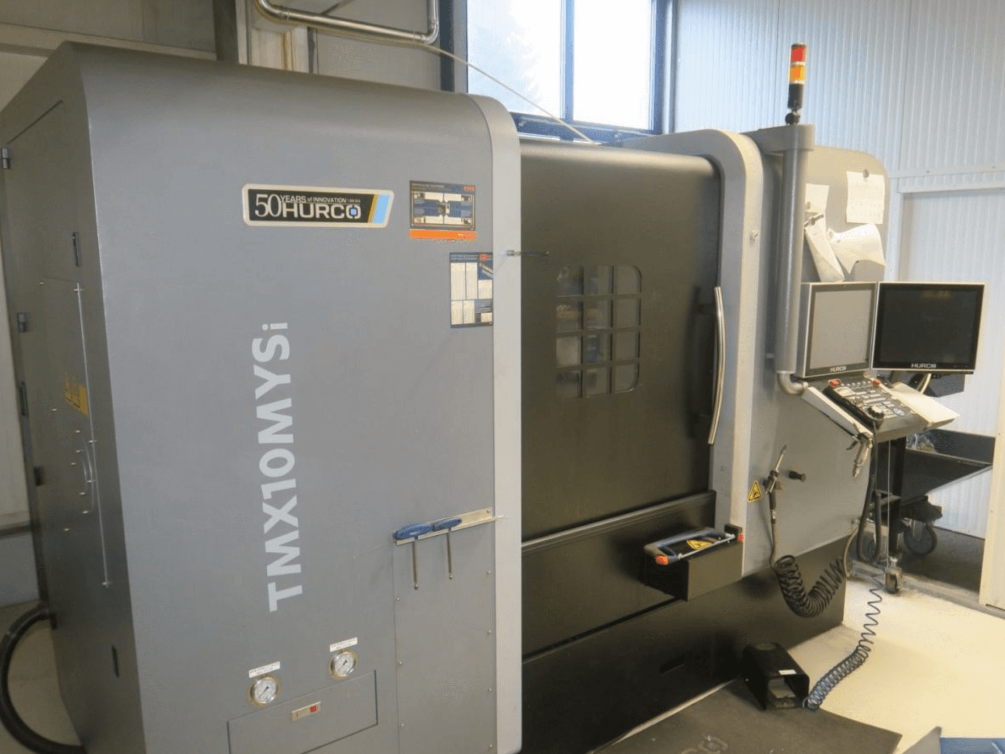 Máquina CNC Hurco TMX10MYSi em vista lateral; possui painel de controlo, luzes de emergência e indicadores apresentados.