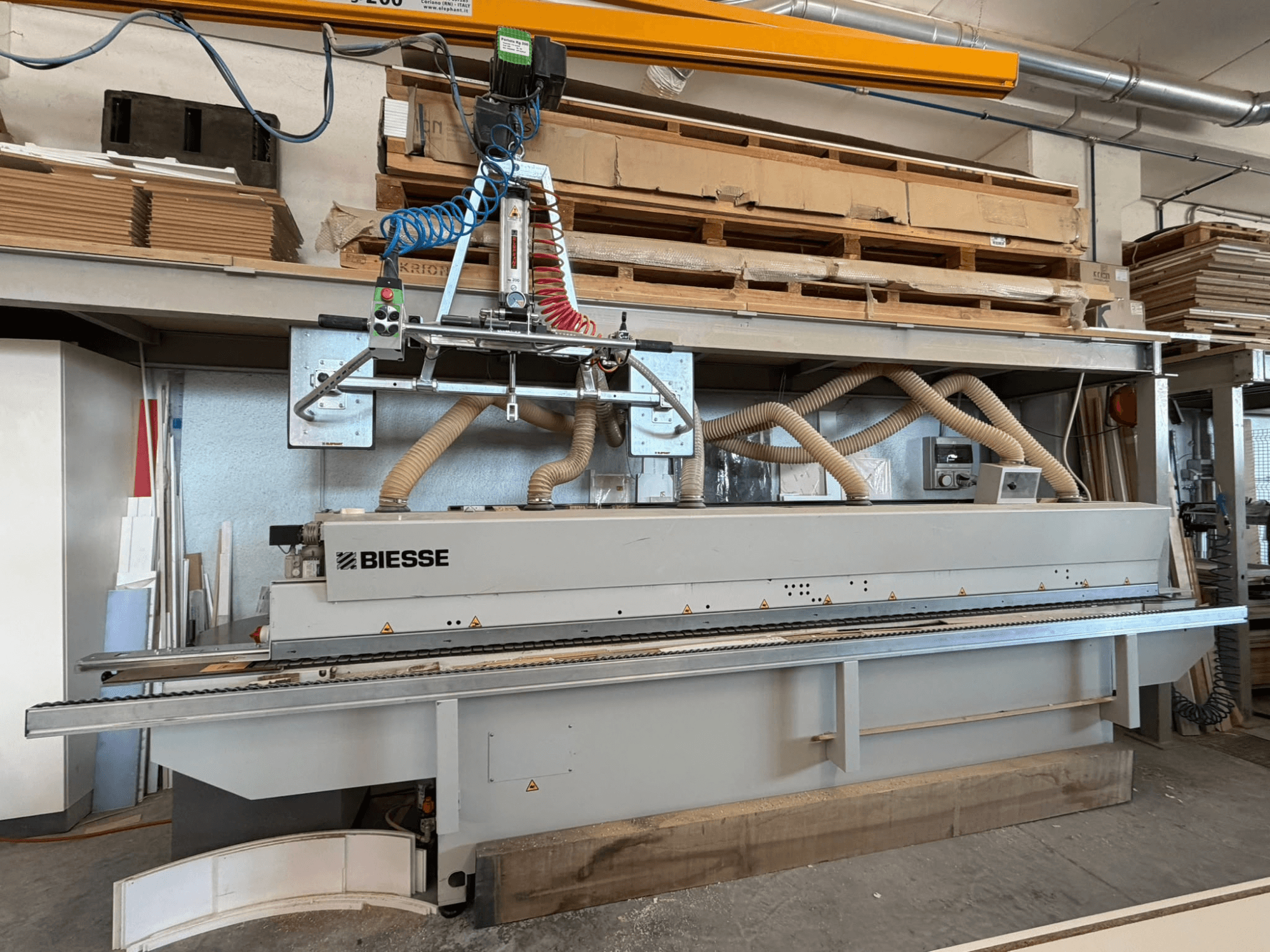 Máquina de encadernação BIESSE AKRON 1330 numa oficina, mostrando a vista frontal com o painel de controlo e o sistema de extração de poeira.