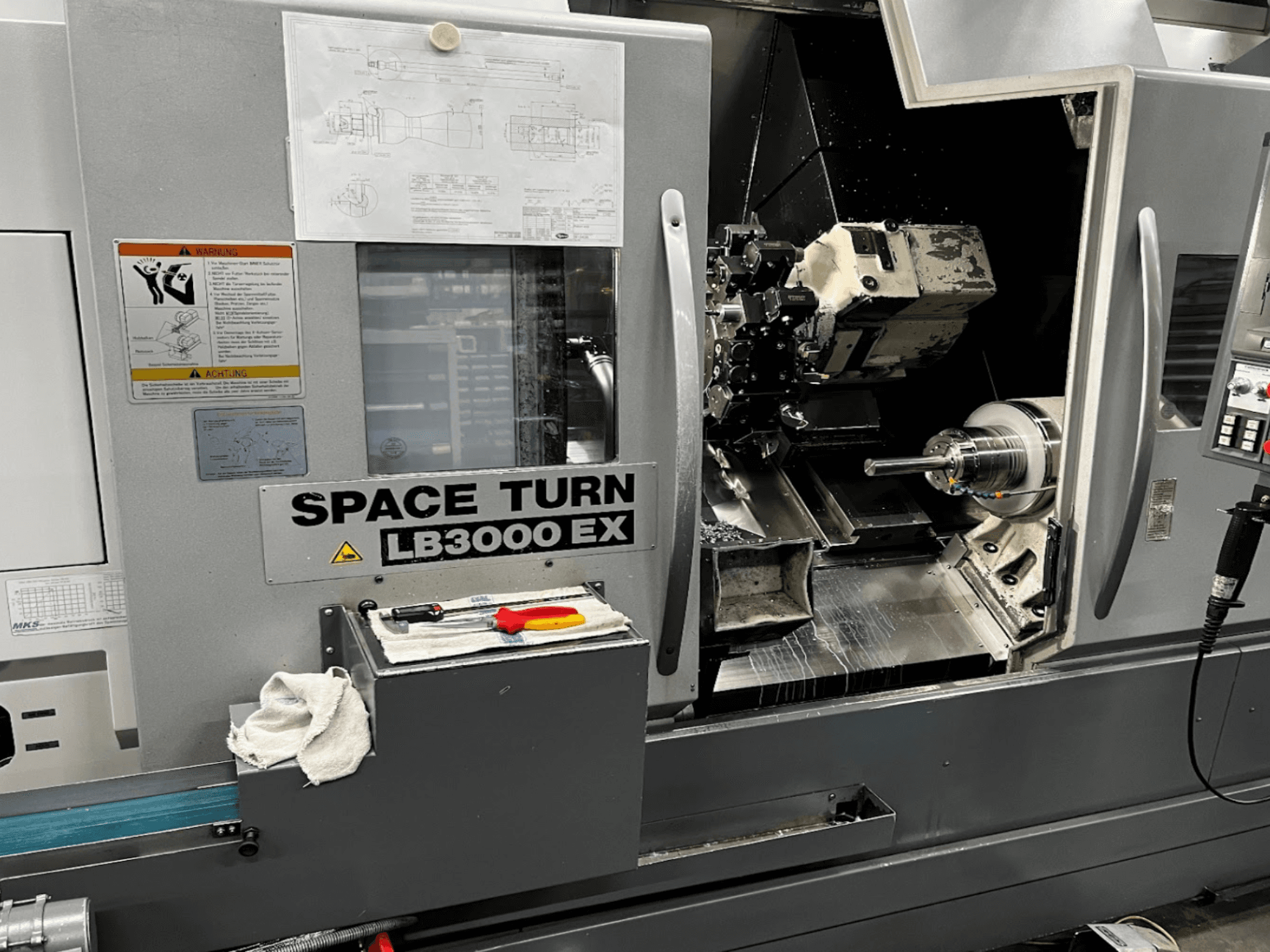 Okuma LB3000EX MYW máquina de tornear horizontal, vista frontal com painel de controlo, ferramentas e detalhes do espaço de trabalho visíveis.