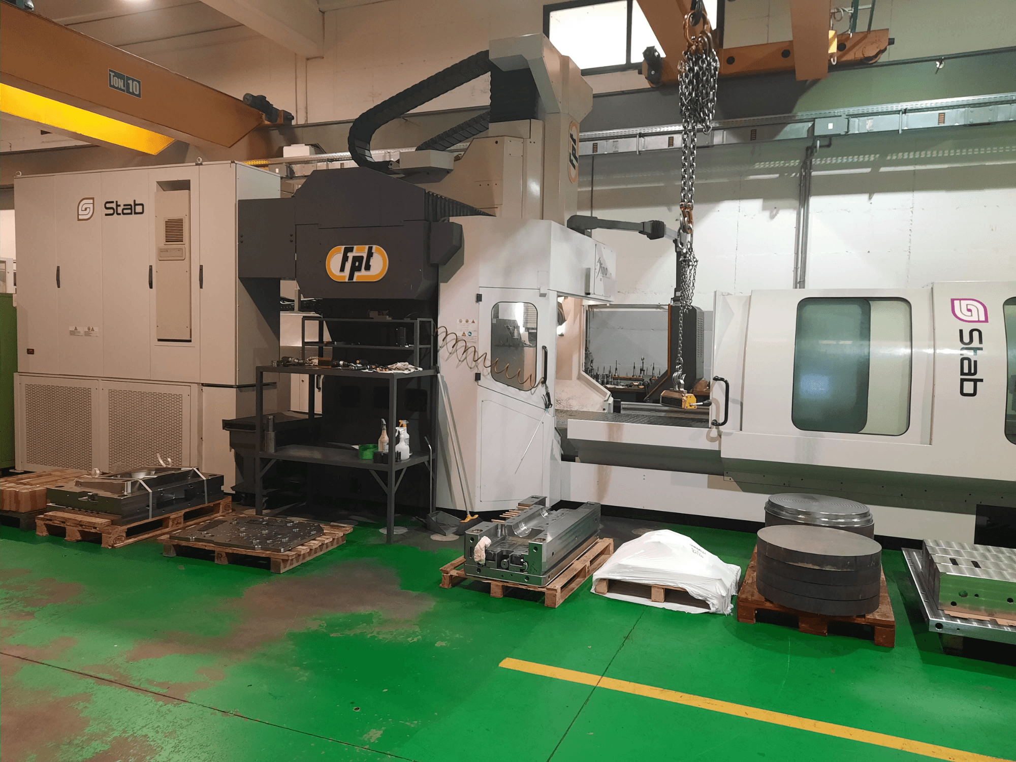 FPT DINO fresadora tipo cama numa oficina, mostrada de uma vista frontal com ferramentas e materiais próximos em paletes.