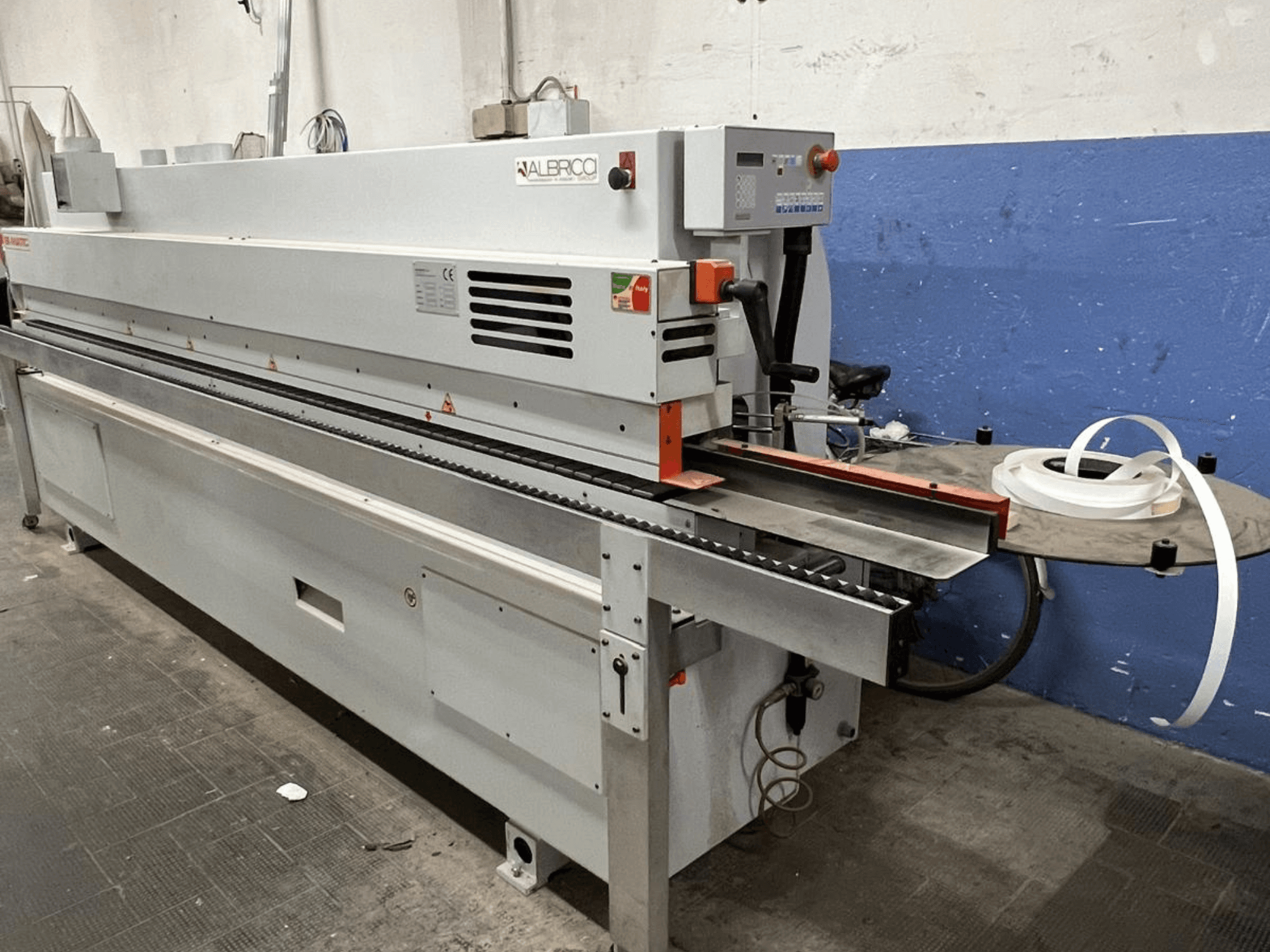 Coladeira de bordos ALBRICO em vista frontal, com um longo tapete transportador e um rolo de fita adesiva.