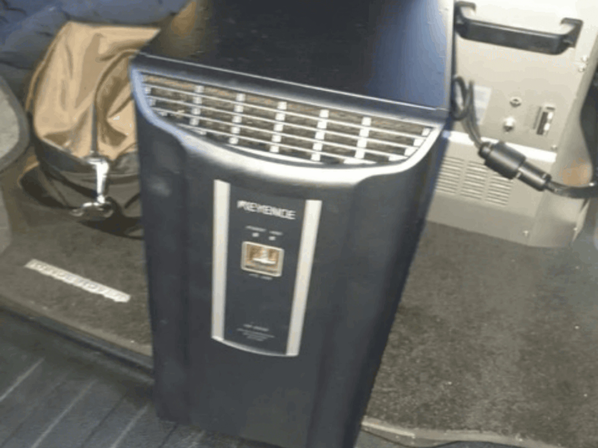 O sistema de automação KEYENCE IM-8030 numa vista frontal, mostrando o painel de controlo e as aberturas de ventilação, tendo como pano de fundo o interior de um veículo.