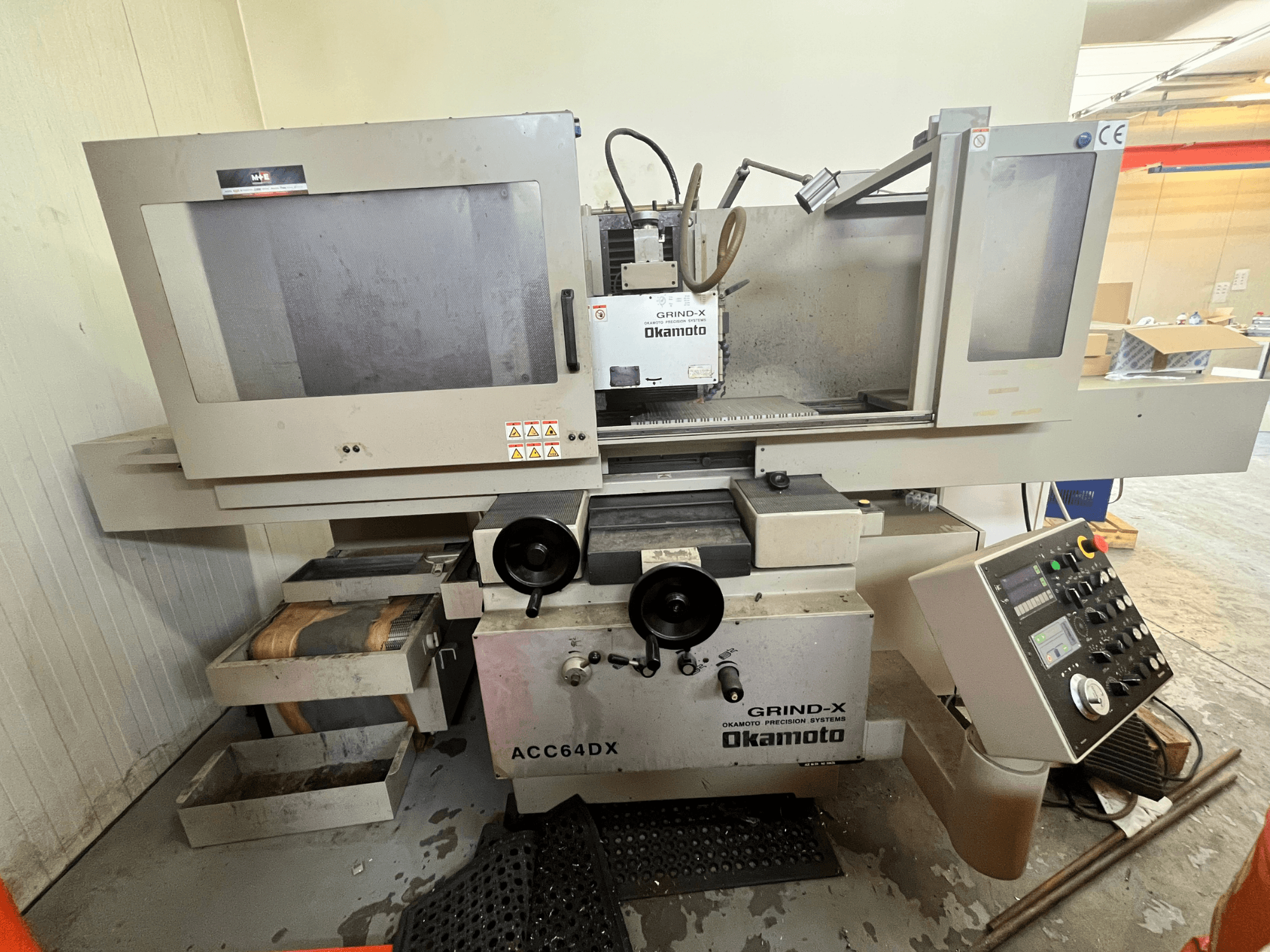 Máquina de retificação plana Okamoto ACC64 DX vista de frente, mostrando o disco de retificação, o painel de controlo e as gavetas de arrumação.