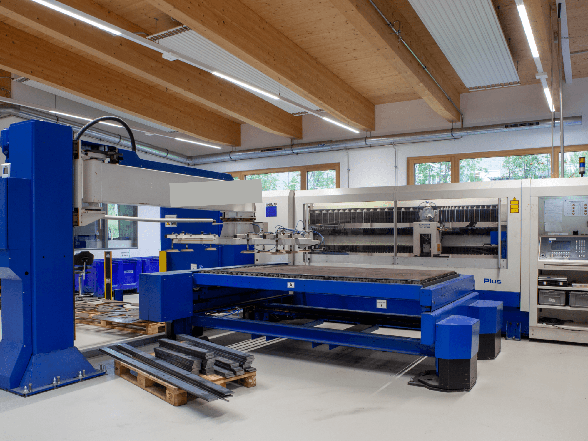 Máquina de corte a laser de CO₂ TRUMPF TRUMATIC L 2530 Plus numa oficina, que se destaca pela sua ampla mesa de corte e pelo seu design industrial.