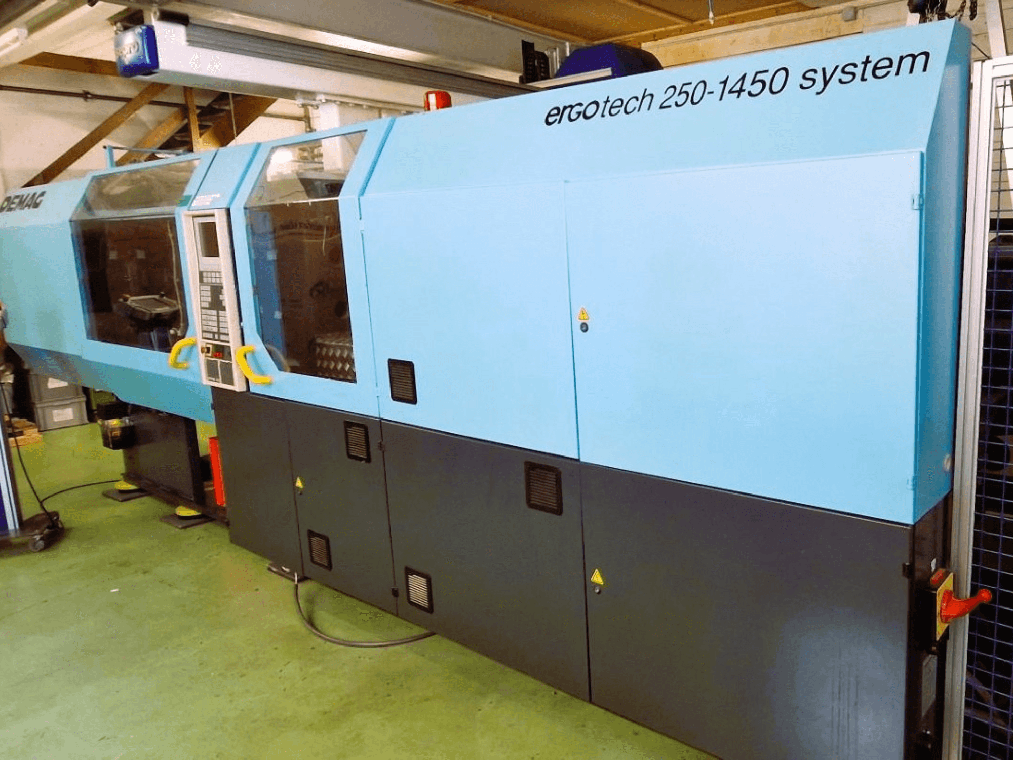 Máquina de moldagem por injeção com sistema Ergotech 250-1450, vista frontal, cor azul e preta, com painel de controlo e caraterísticas de segurança visíveis.