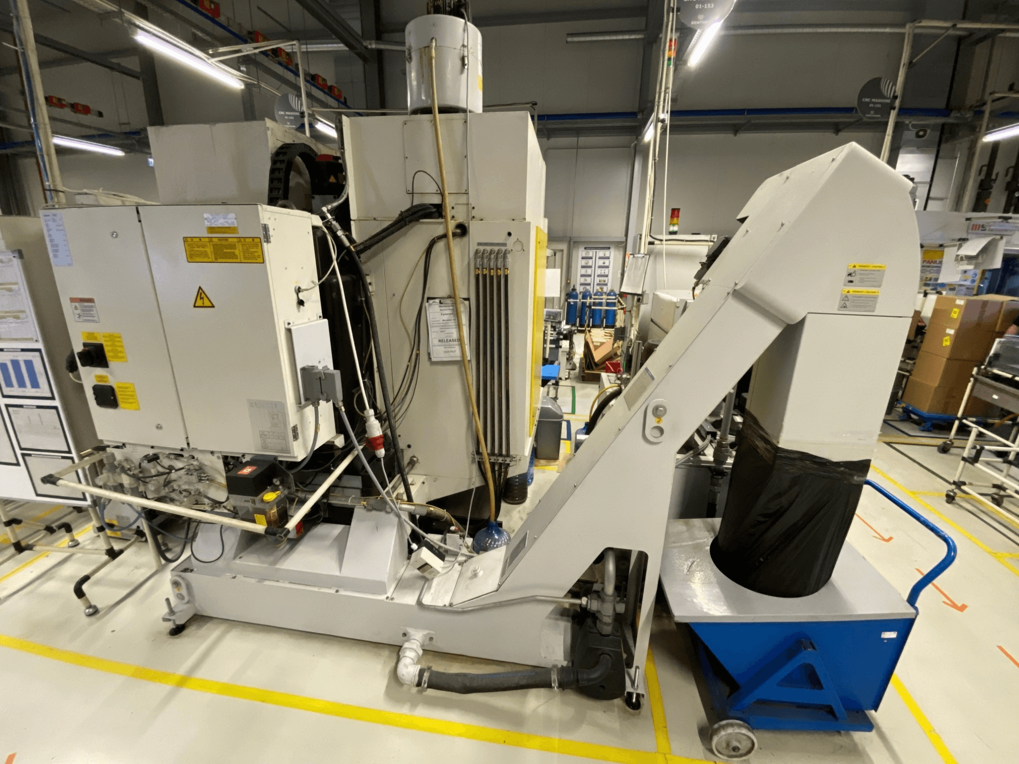 Vista frontal do centro de maquinagem vertical FANUC ROBODRILL α-D21LiB, mostrando os componentes elétricos e a calha de saída.
