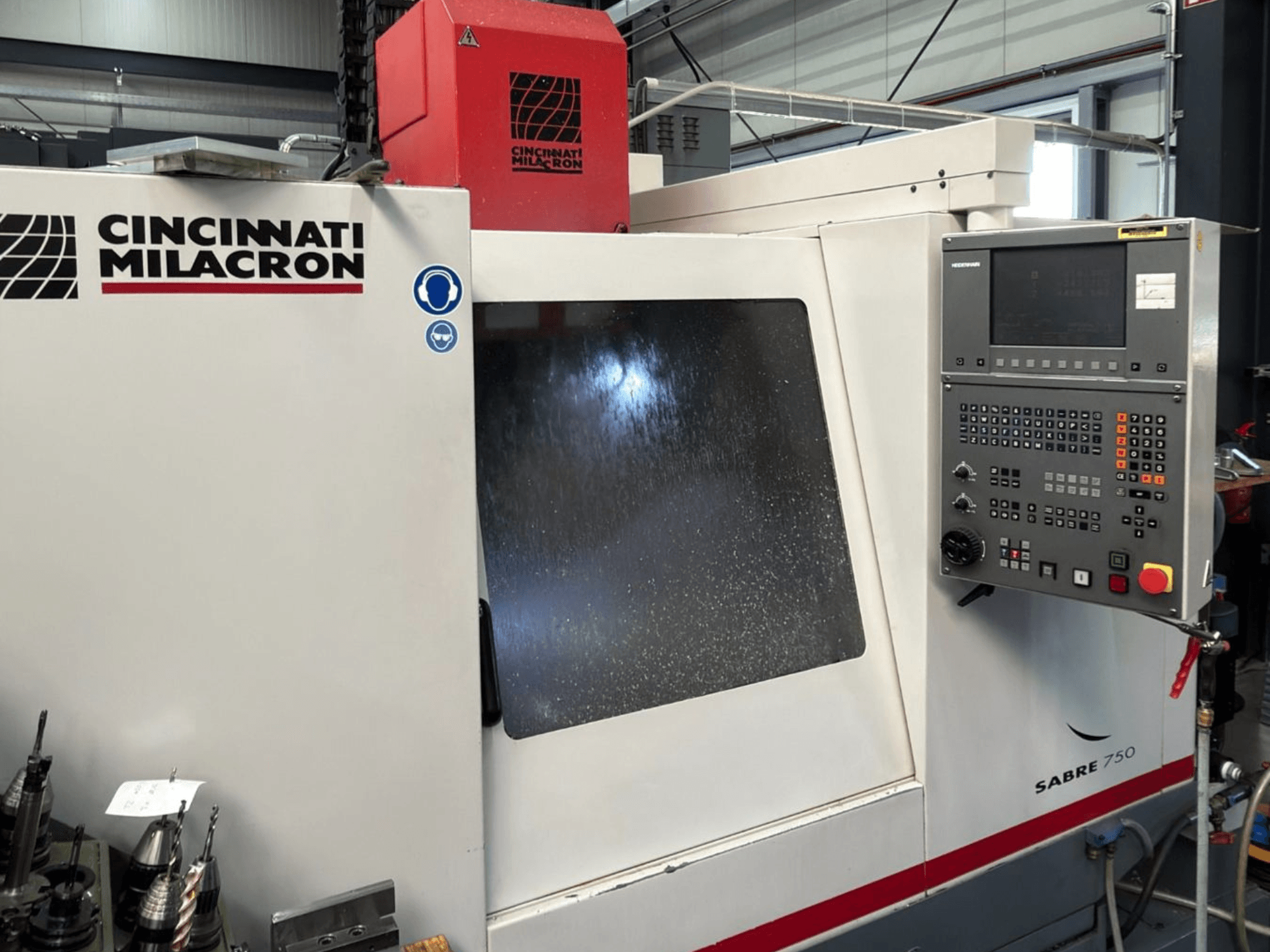 Centro de maquinagem vertical Cincinnati Milacron Sabre 750, vista frontal, com painel de controlo e vidro parcialmente oculto.