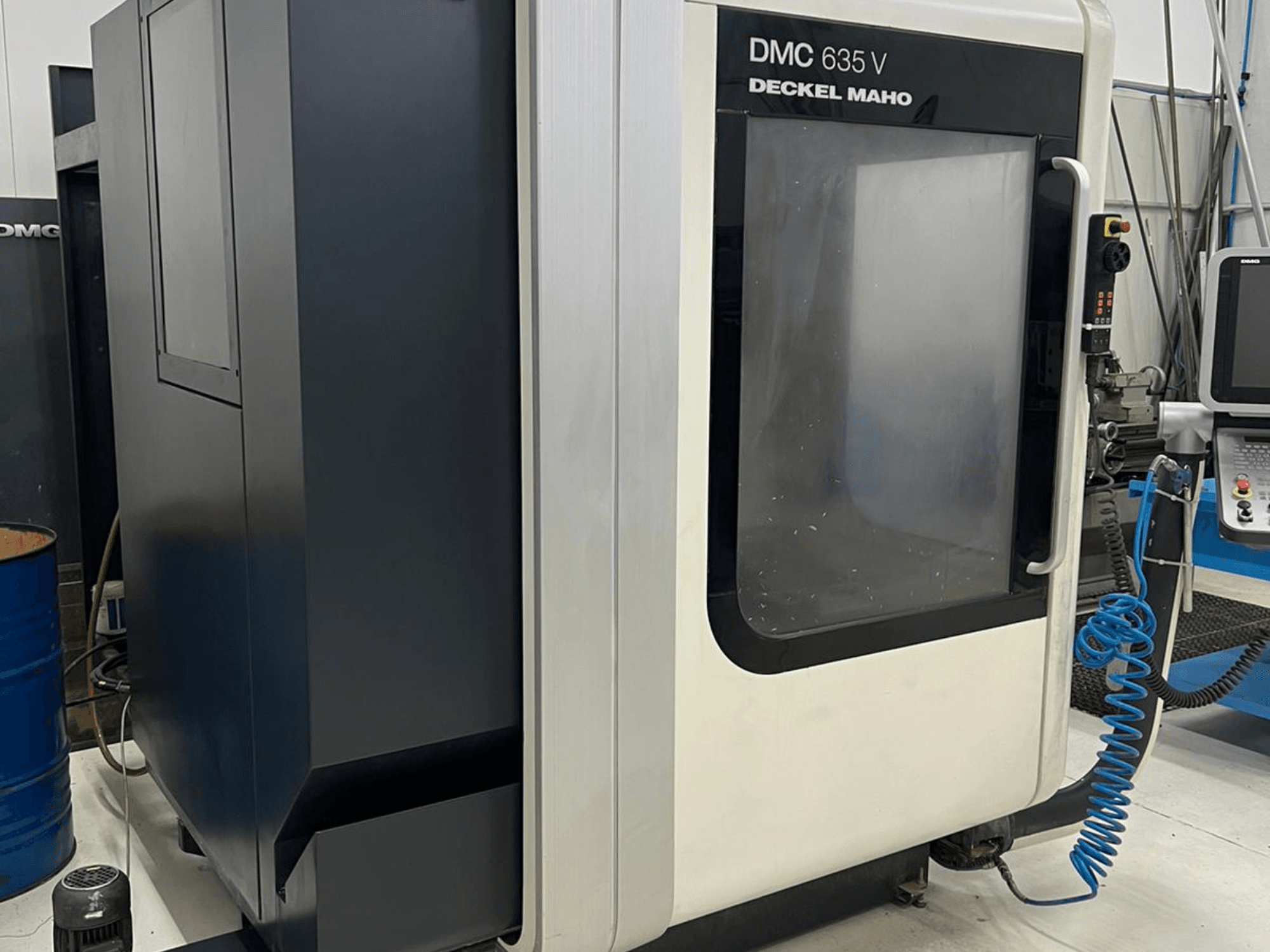 Fresadora DMC 635 V da Deckel Maho, vista lateral mostrando o painel de controlo e a porta de acesso parcialmente aberta.