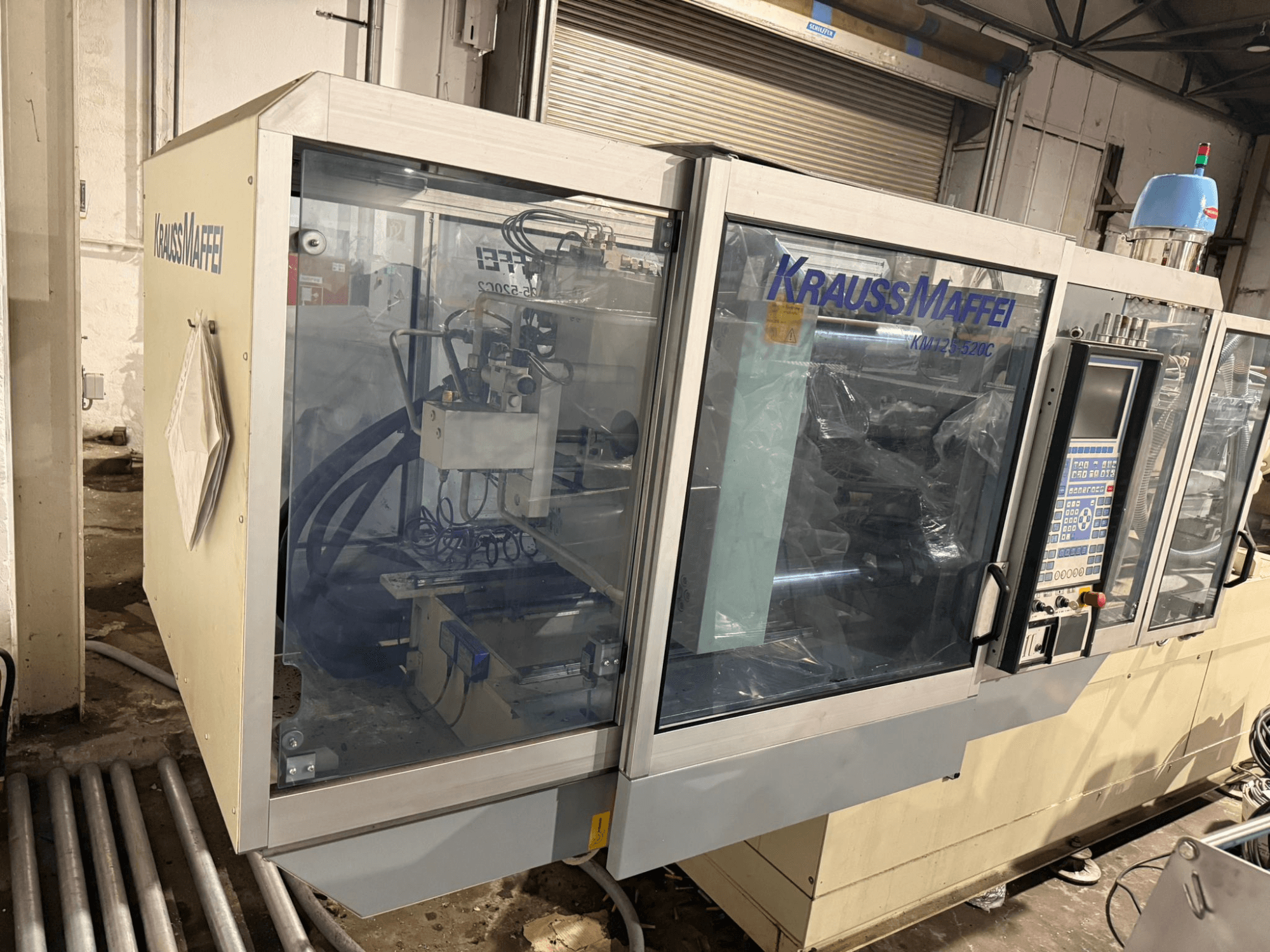Máquina de moldagem por injeção hidráulica Krauss Maffei KM125-520C2, vista frontal com painel de controlo e caixa transparente.