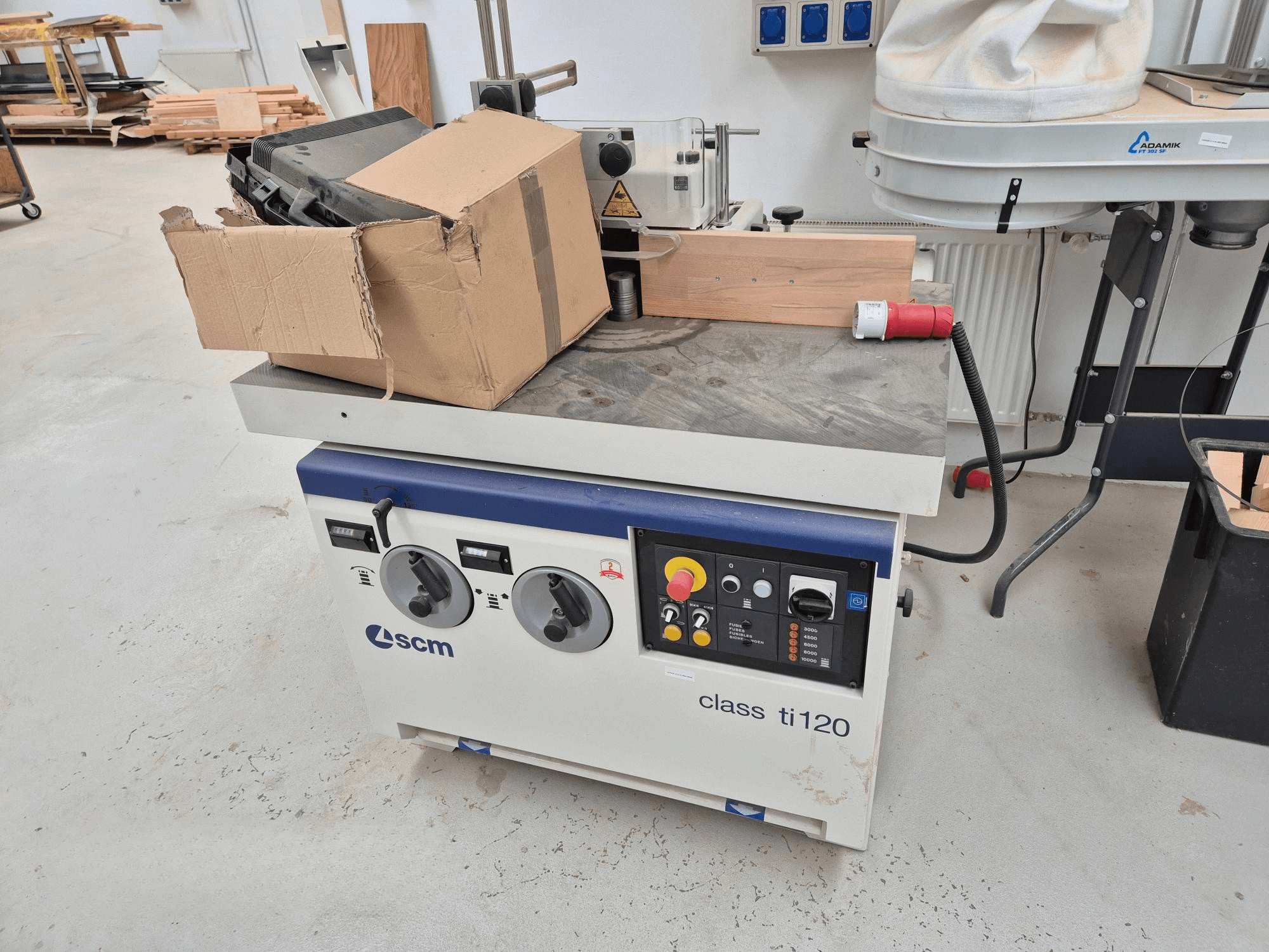 Máquina para trabalhar madeira SCM classe ti120, vista frontal, com um painel de controlo com botões e botões, e uma caixa de cartão anexa.