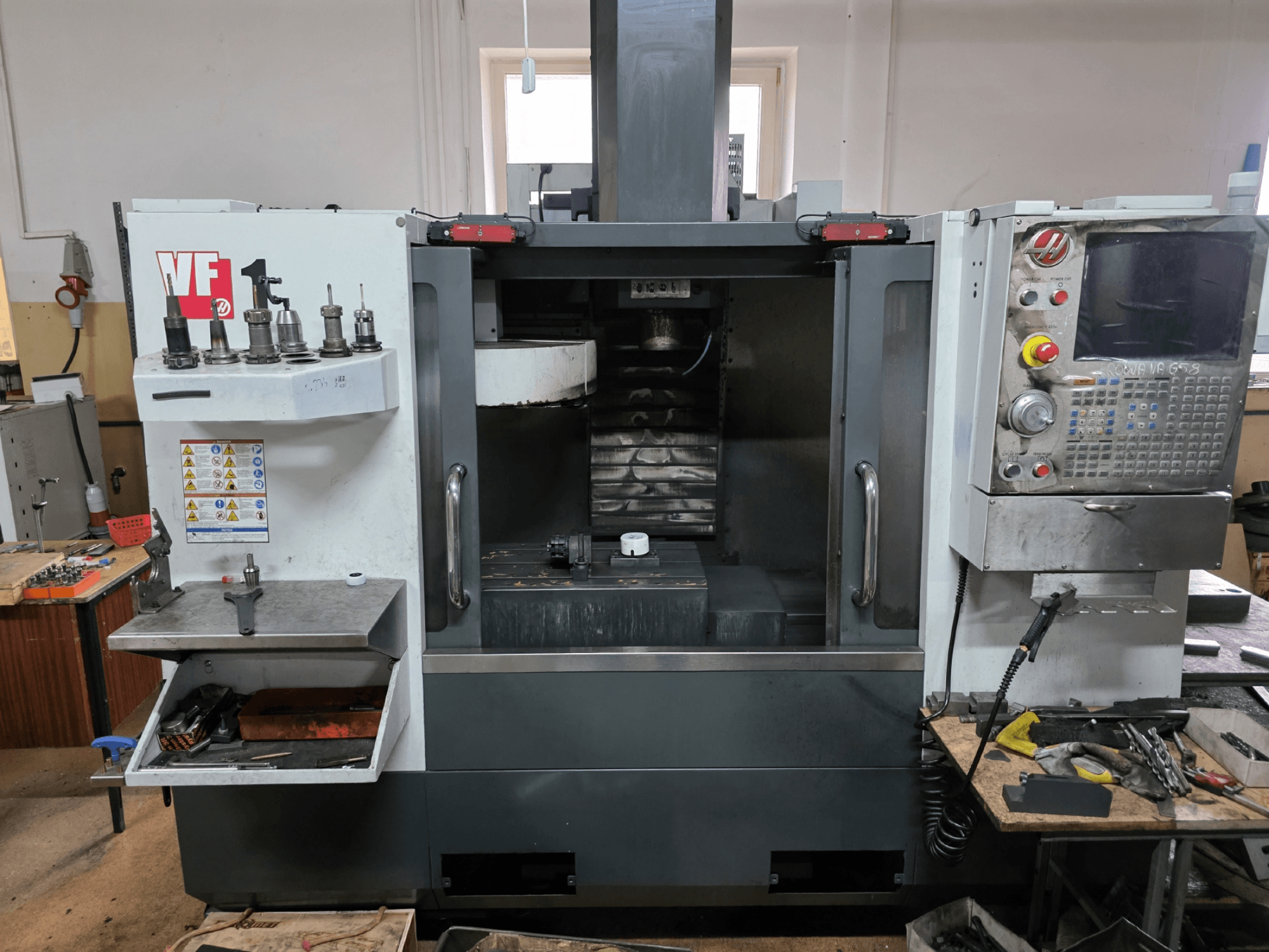 Fresadora CNC Haas série VF, vista frontal; possui vários suportes de ferramentas, painel de controlo e área de trabalho visível.