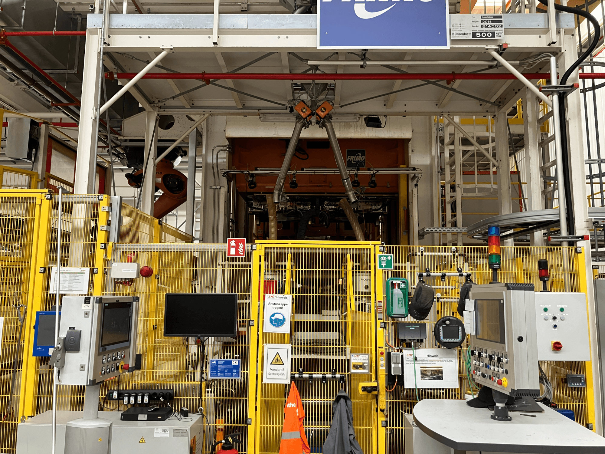 Vista frontal da fábrica de termoformagem FRIMO NFPP, com painéis de controlo e vedações de segurança num ambiente industrial bem iluminado.
