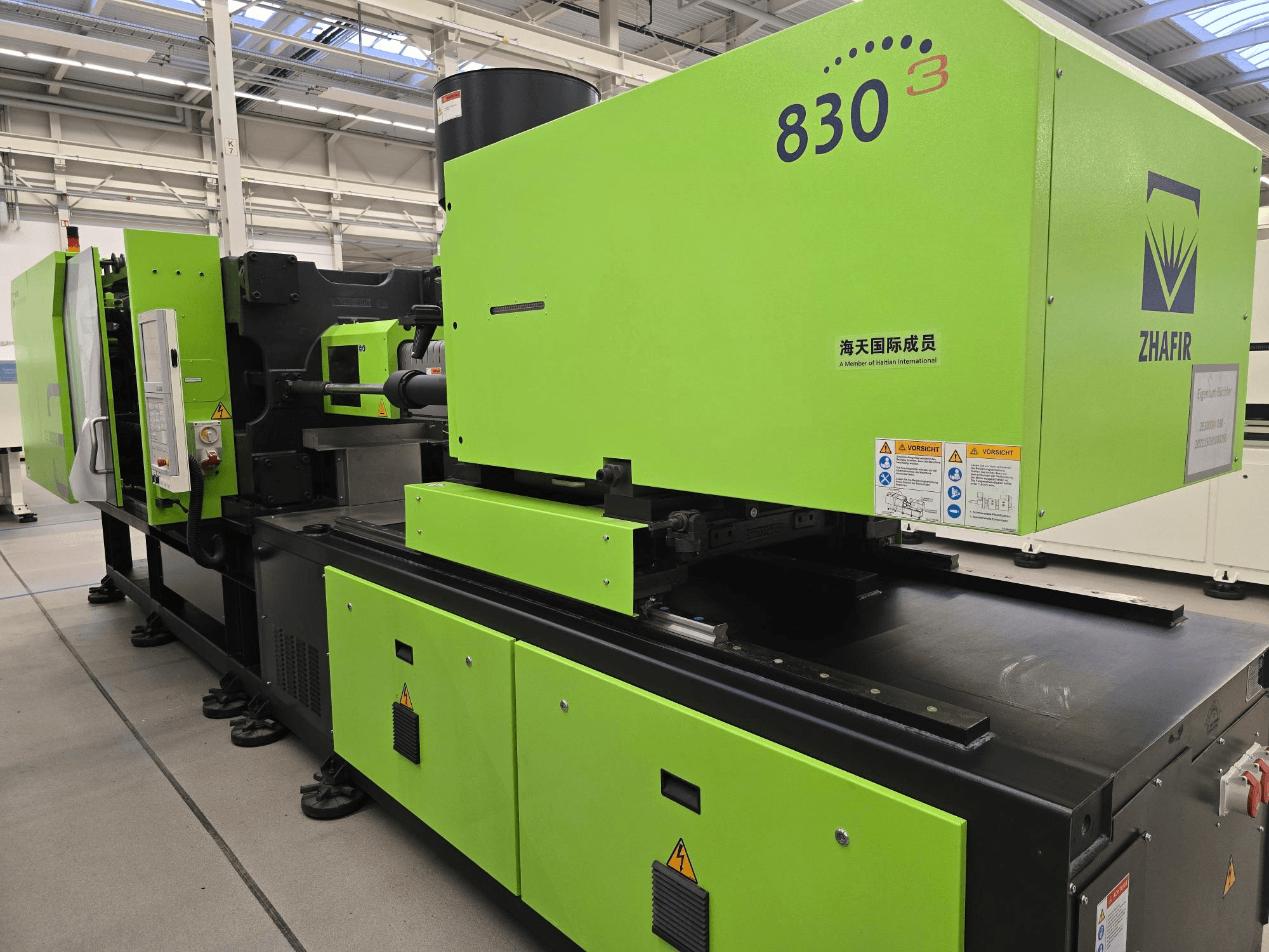 Máquina de moldagem por injeção eléctrica ZHAFIR ZERES III 3000/830/B5, vista lateral, com a caixa verde brilhante e o painel de controlo visível.
