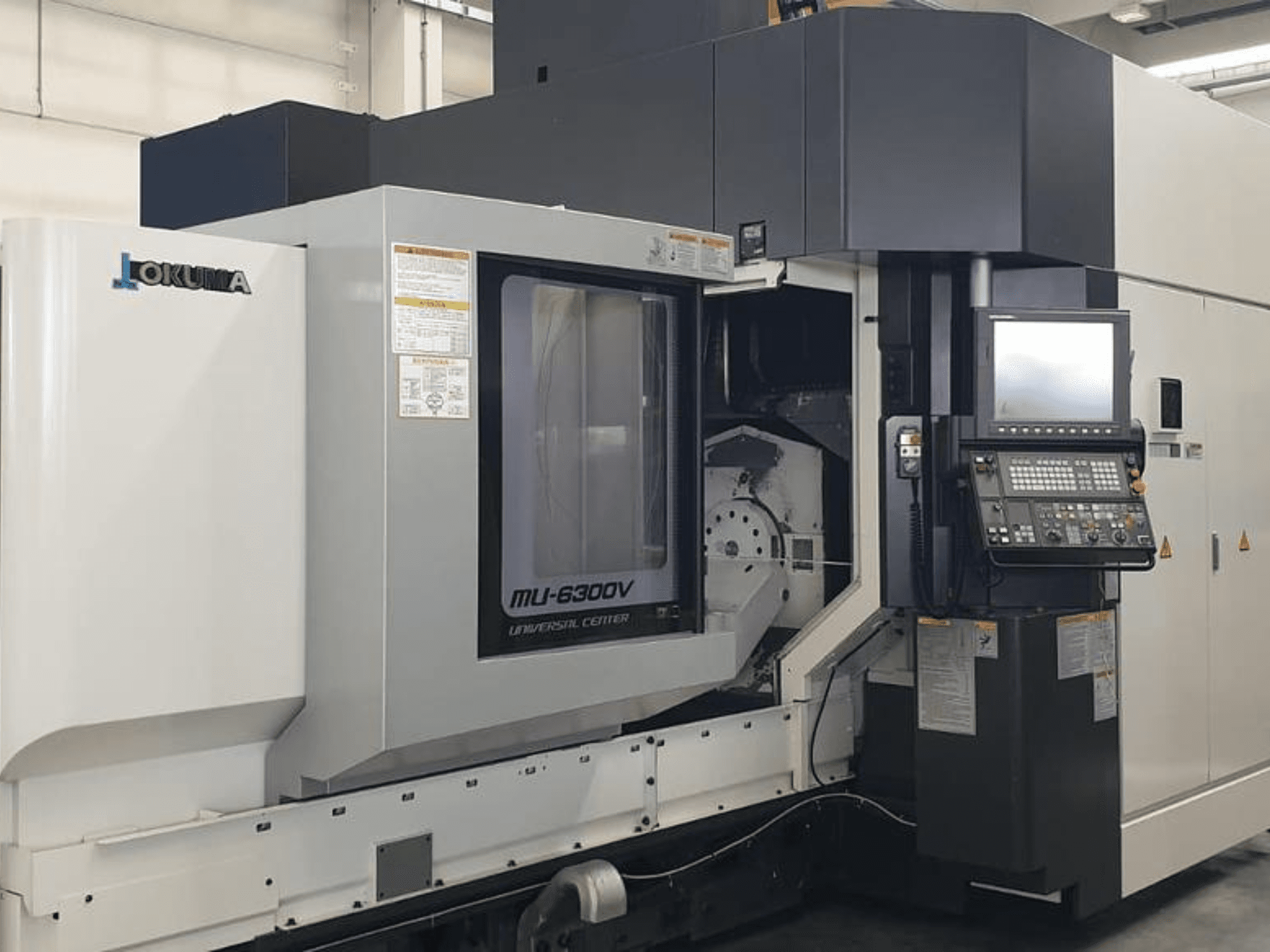 Centro de maquinação vertical Okuma MU 6300 V, vista frontal mostrando o painel de controlo e os detalhes da área de maquinação.