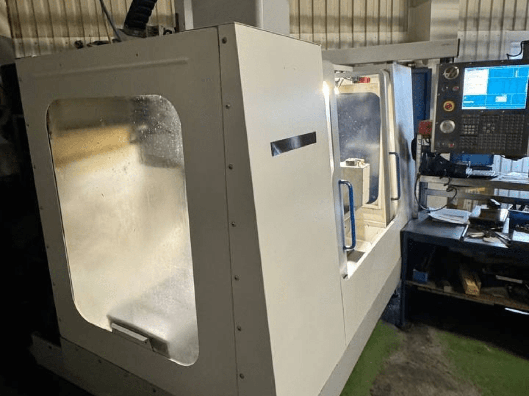 Centro de Maquinação Vertical HAAS VCE 750 em vista lateral, com um painel de controlo e uma caixa de segurança transparente.