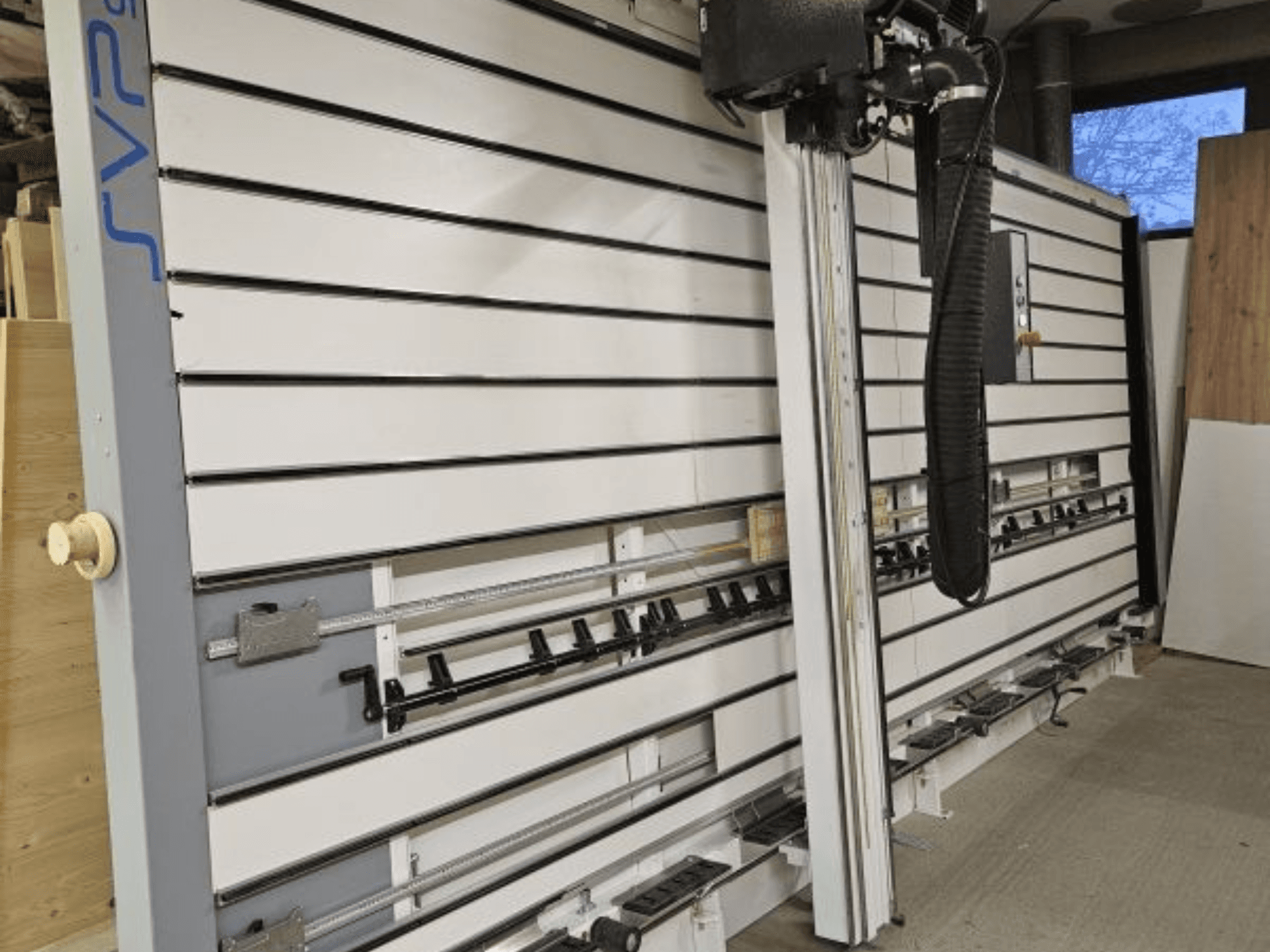 Serra de painel deslizante SVP numa oficina, vista frontal, com calhas ajustáveis e um sistema de extração de poeiras suspenso.