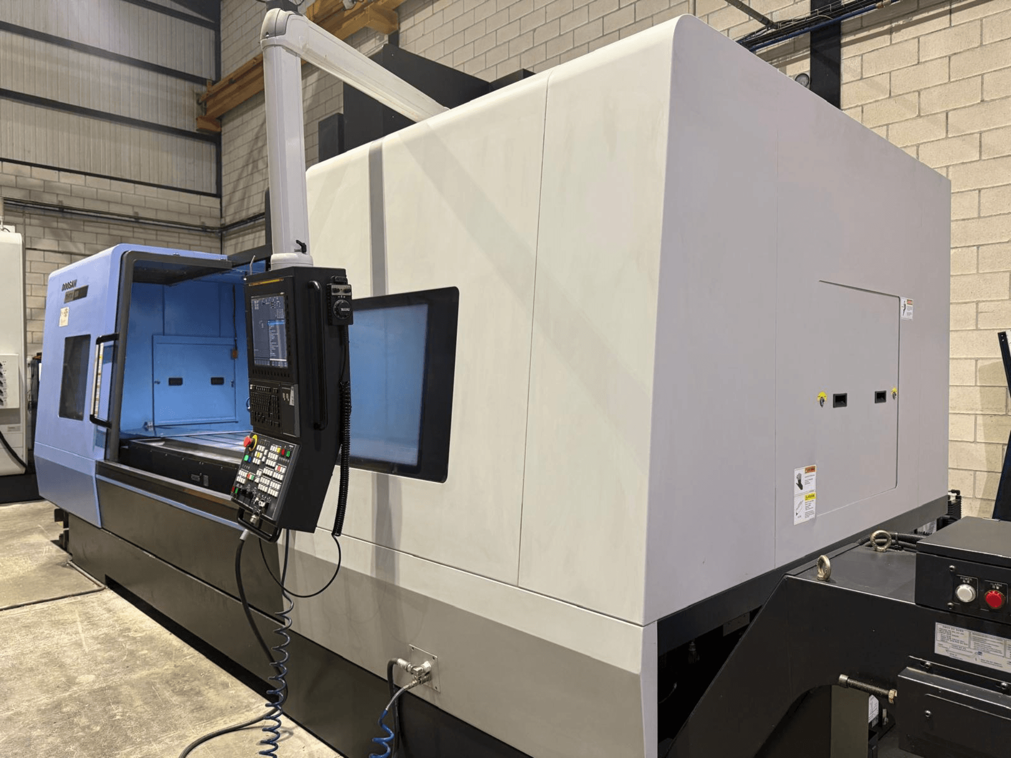 Torno CNC industrial, exterior azul e cinzento, vista frontal; possui painel de controlo com botões e visor para operações precisas.