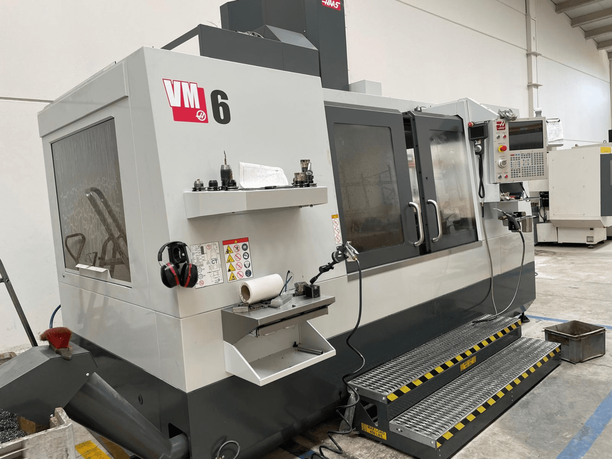 Centro de maquinação vertical Haas VM-6, vista frontal mostrando o painel de controlo, suportes de ferramentas e caraterísticas de segurança.