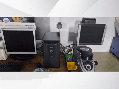 Dois monitores de computador, um Acer e um Keyence, ao lado de um dispositivo preto e de um microscópio, vistos de frente.