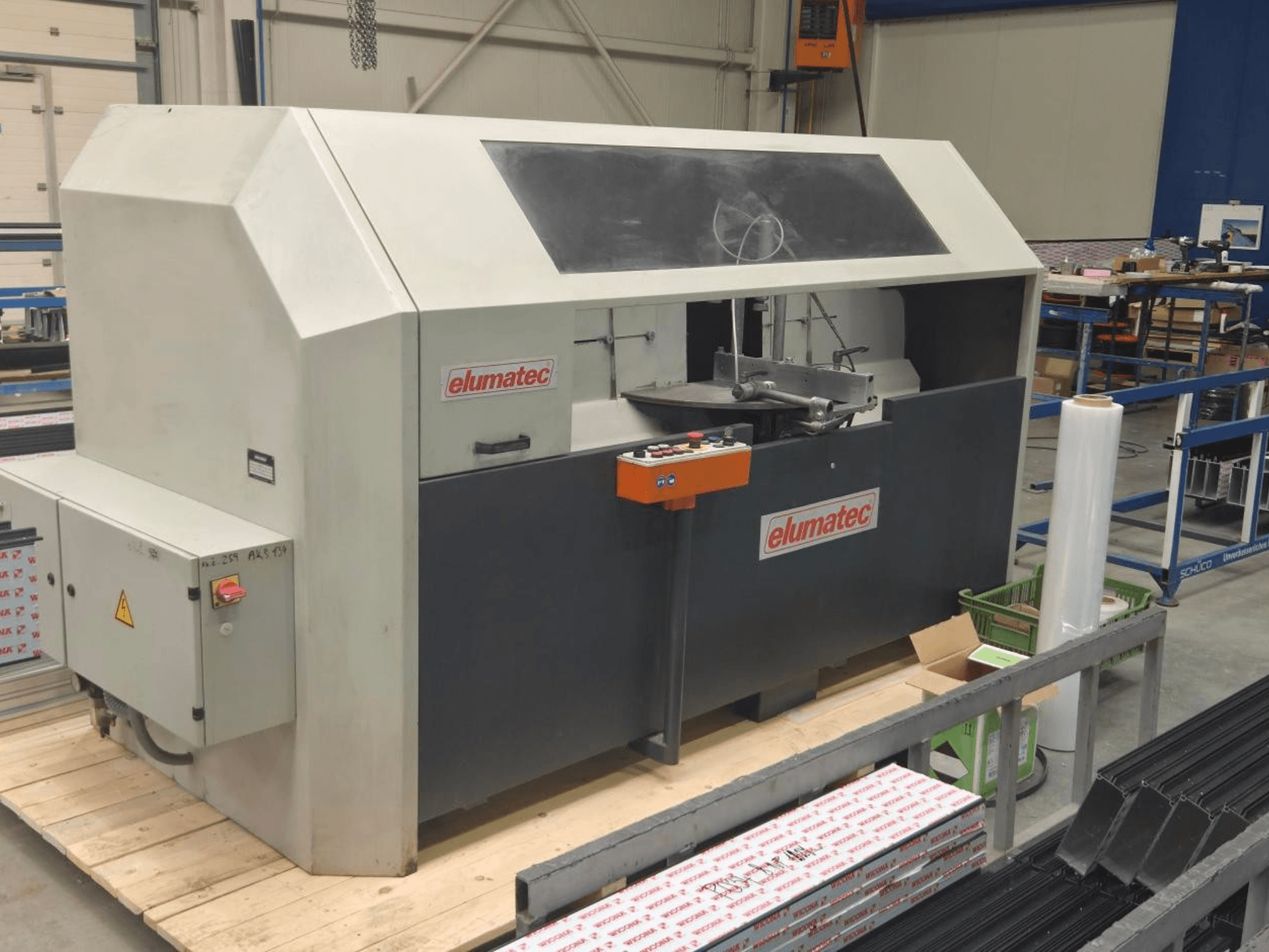 Serra circular para metal Elumatec AKS 134, vista frontal, mostrando o painel de controlo e a área de corte numa plataforma de madeira.