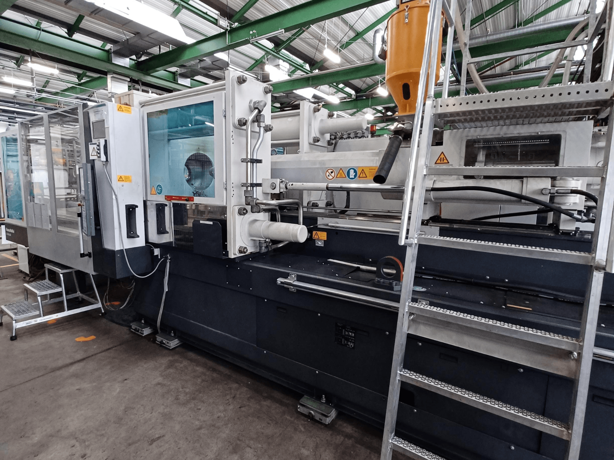 Máquina de moldagem por injeção industrial com uma vista frontal clara, mostrando as marcas, o painel de controlo e a tremonha de material.