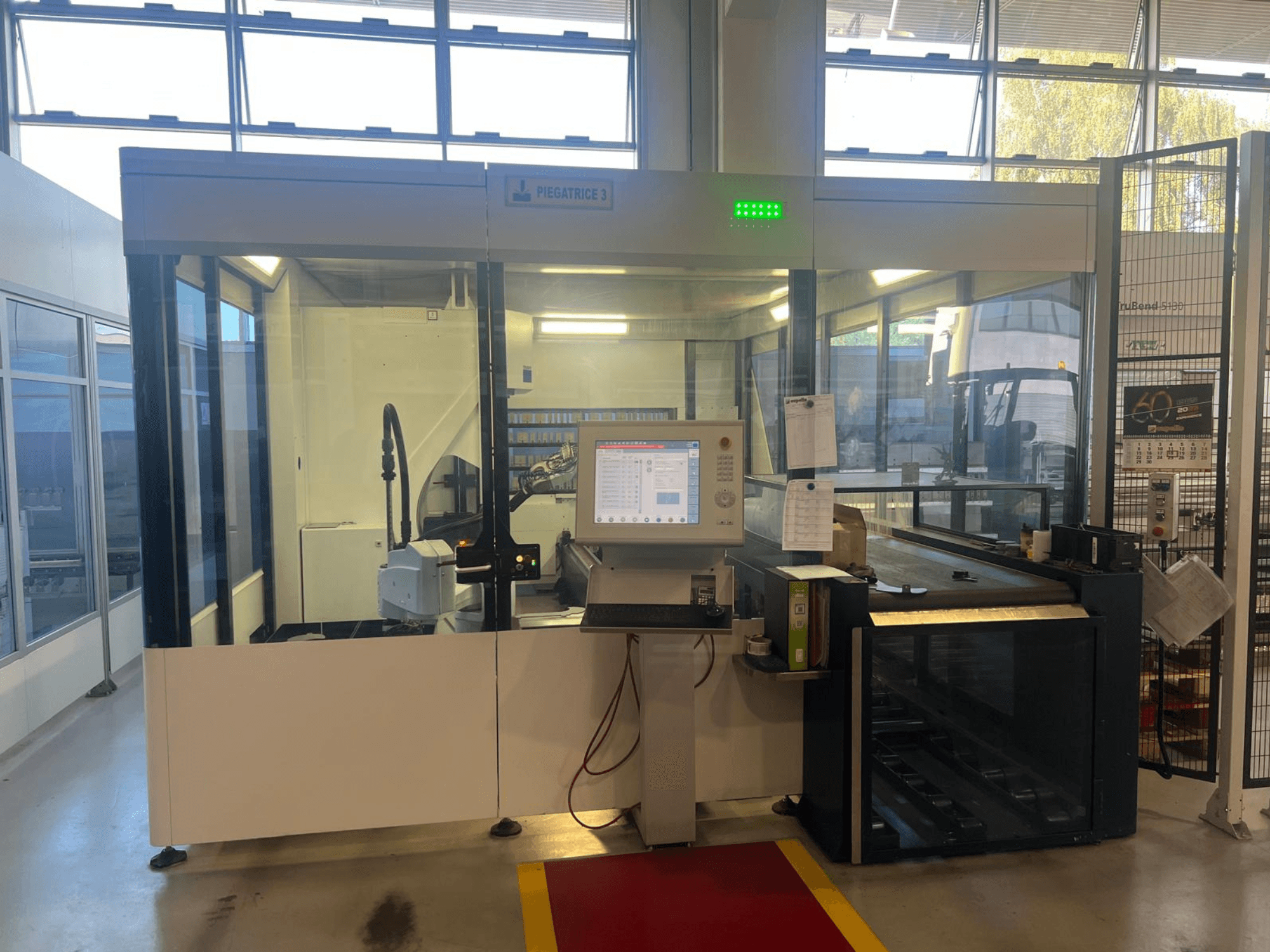 Máquina de dobragem industrial, modelo Piegatrice 3, vista frontal com painel de controlo e braço robótico, numa oficina bem iluminada.