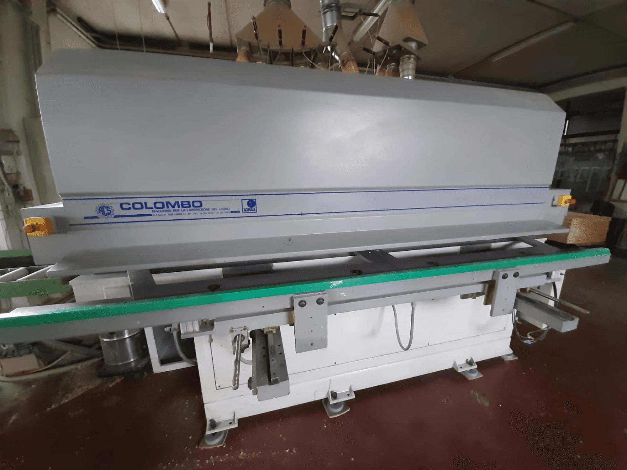 Máquina de processamento de madeira Colombo, vista frontal, com uma longa mesa verde, botões de controlo e um corpo cinzento com detalhes em azul.