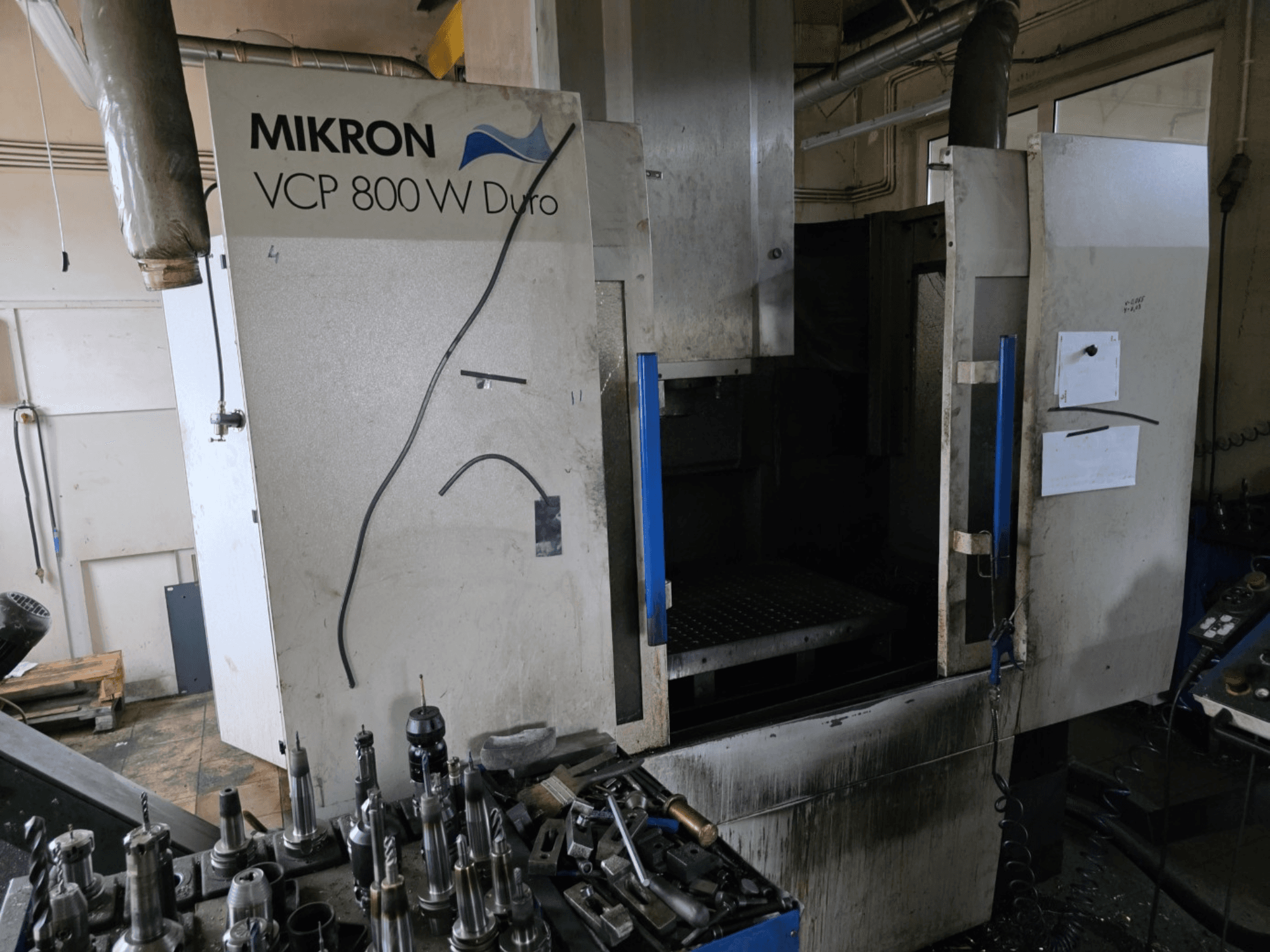 Fresadora Mikron VCP 800 W Duro vista de lado, com ferramentas e comandos visíveis em primeiro plano.