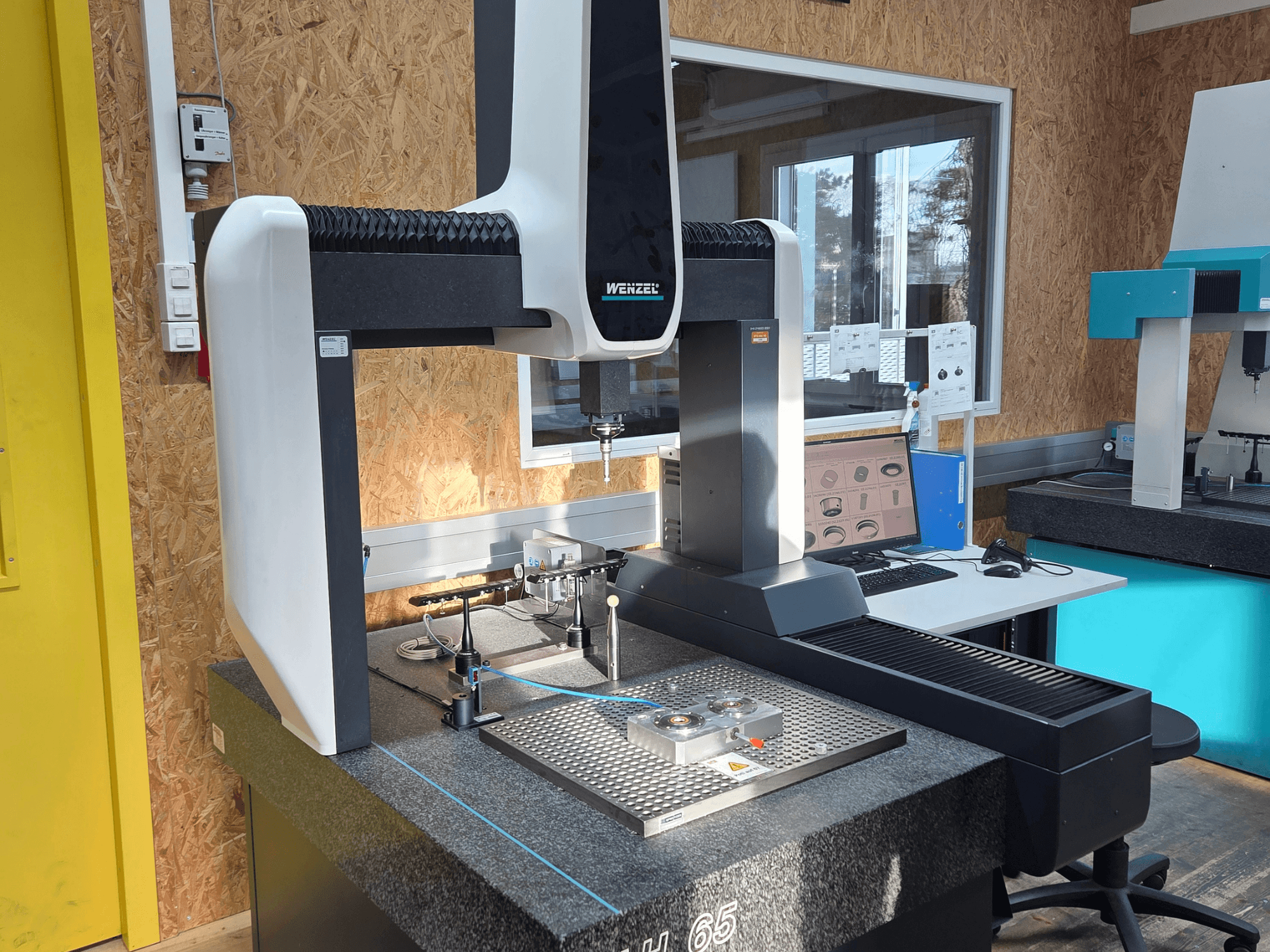 Máquina de medição por coordenadas Wenzel LH 65 numa configuração de laboratório, vista frontal, com ferramentas de medição e um monitor.